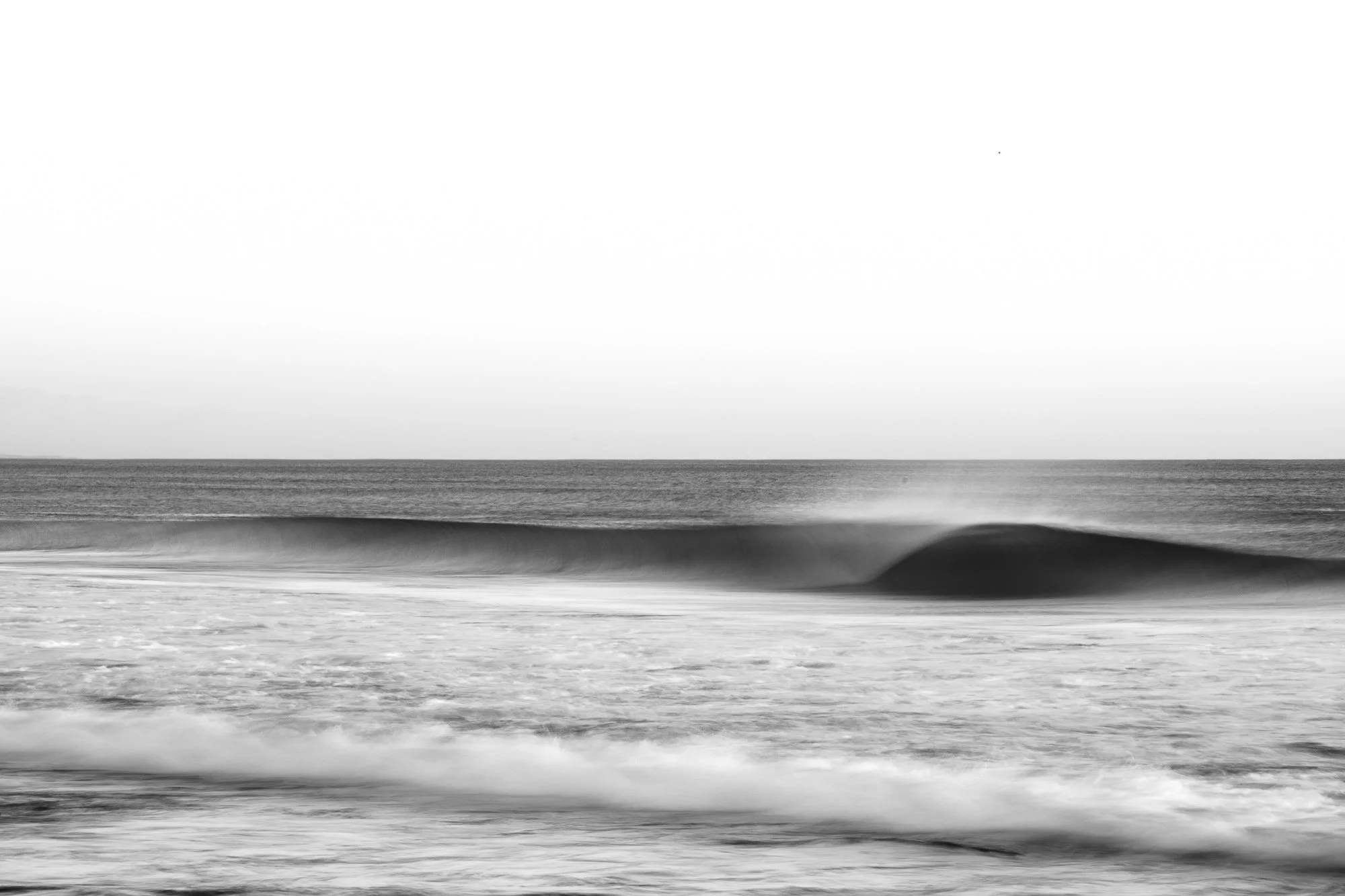 Una ola solitaria se desliza en blur motion, convertida en una forma abstracta donde el movimiento lo es todo. Ya no se percibe como agua definida, sino como una masa fluida que se estira y se disuelve en el encuadre, creando líneas suaves y transici