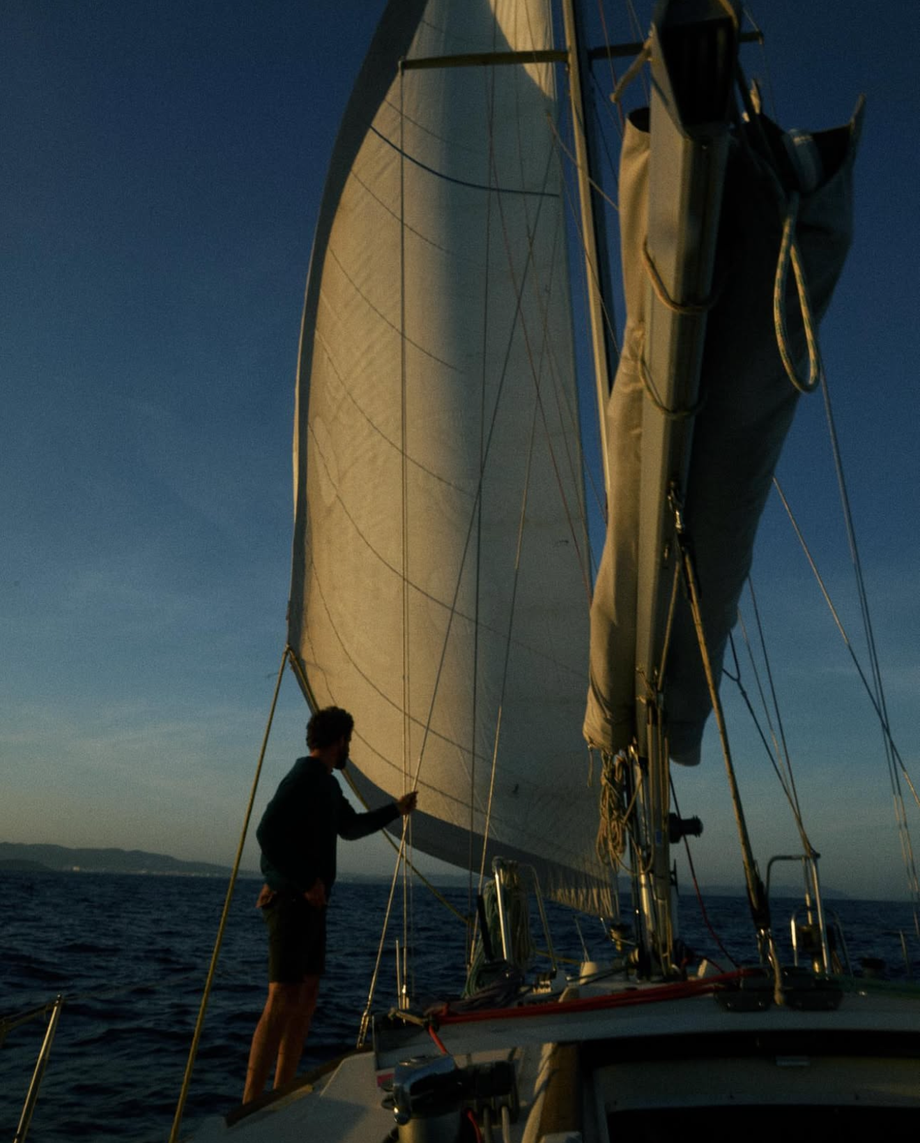 Un hombre ajustando las velas de un yate en el mar durante el atardecer.