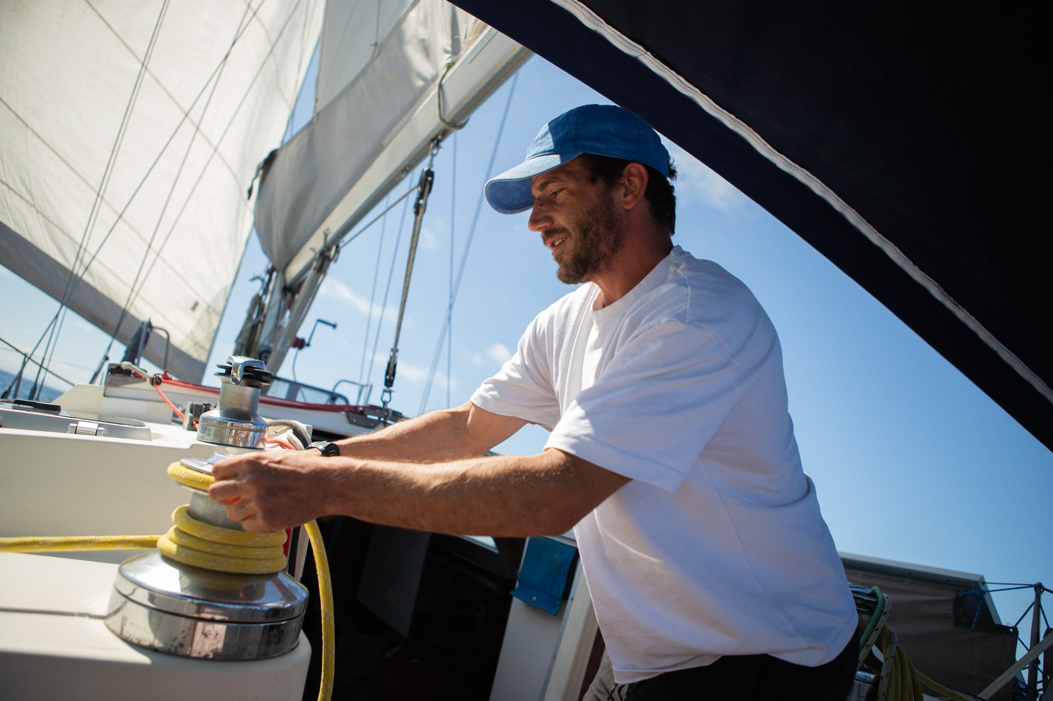 Hombre ajustando una cuerda en una embarcación de vela en un día soleado.