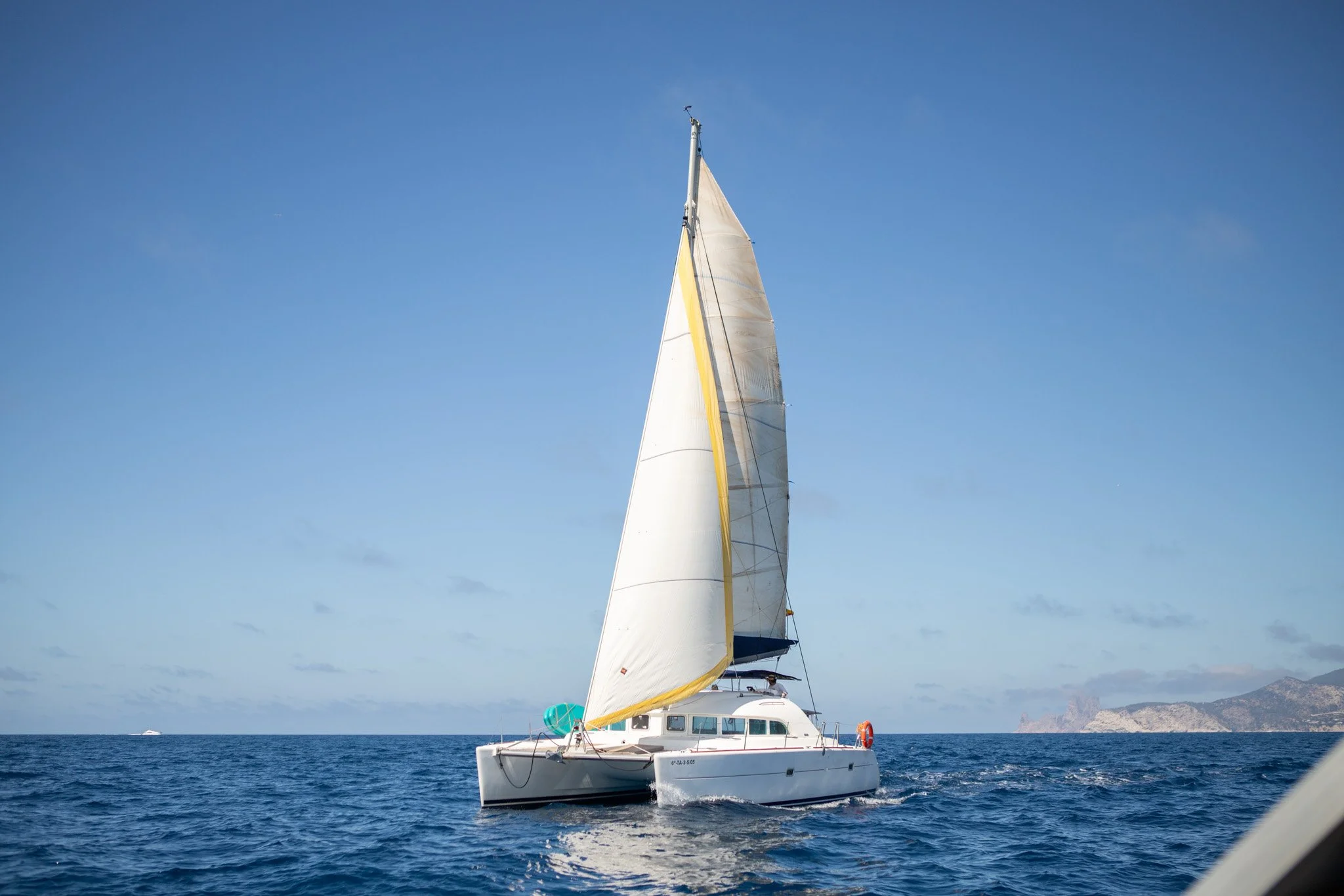 Un catamarán navegando en el mar con un cielo despejado y montañas en el fondo.