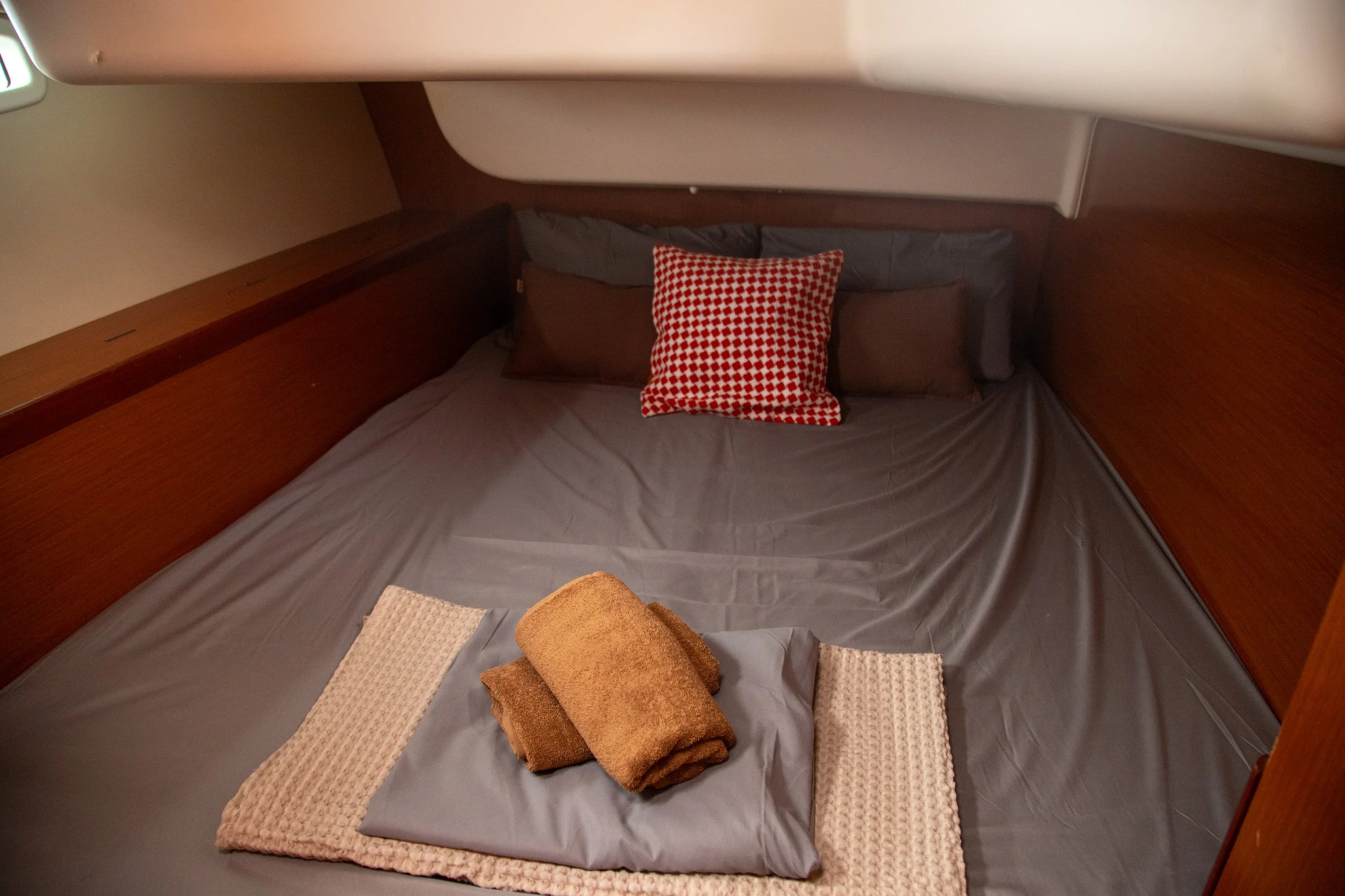 Recámara con cama, almohada, cobija y cortina de madera en un interior de barco o casa flotante, con madera en paredes, suelo y muebles.