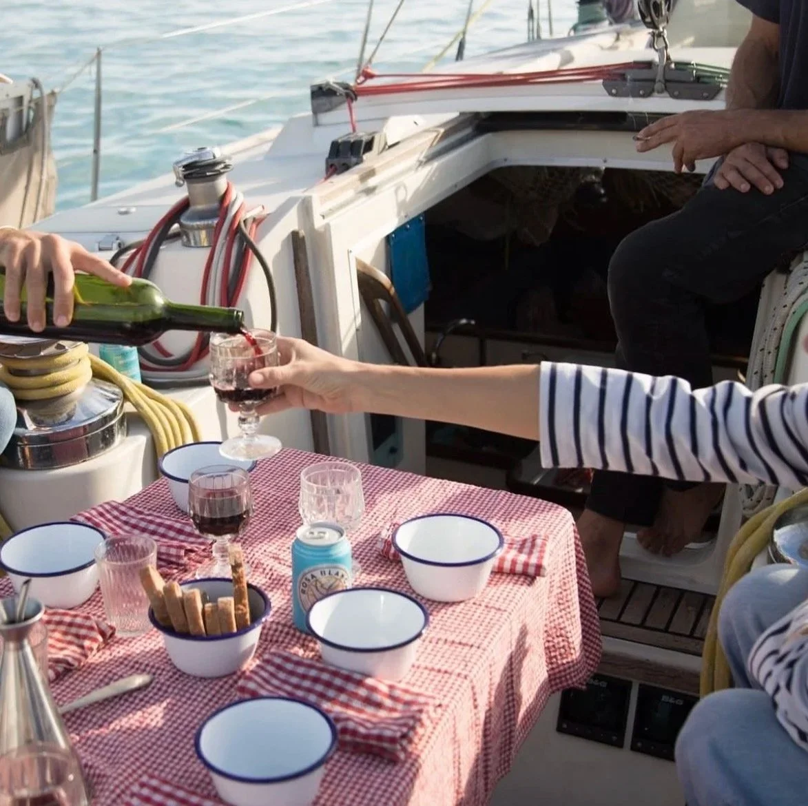 Personas sirviendo vino en un yate con mesa puesta con platos, vasos y galletas.