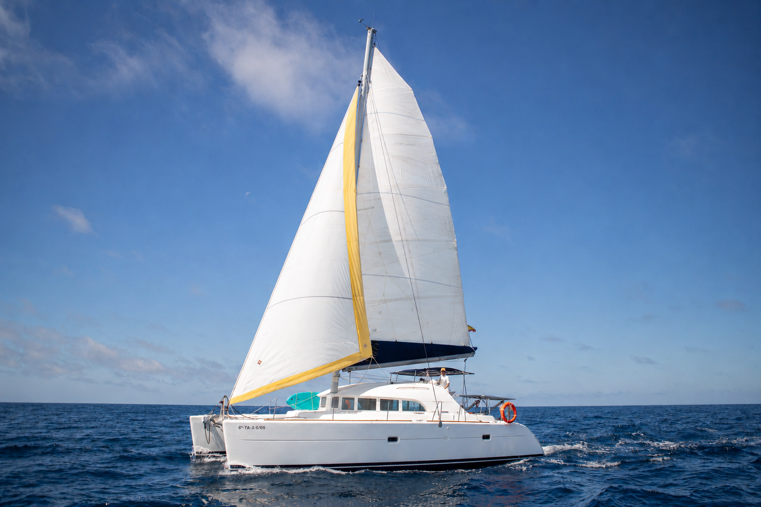 Velero blanco navegando en el mar, con cielo despejado y algunas nubes.