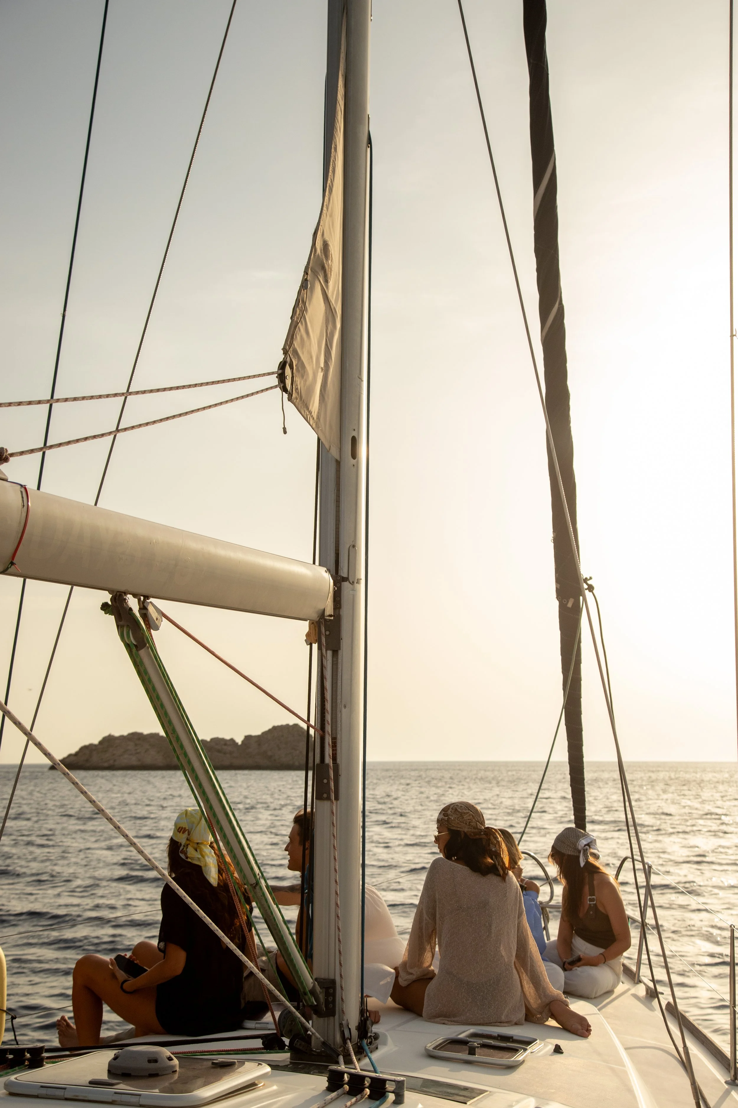 Mesa con mantel de cuadros rojos y blancos, dos copas con vino tinto, una botella de vino, uvas verdes, un cuchillo y almendras en una tabla sobre un barco en el mar con cuerda enrollada y espacio para navegar.