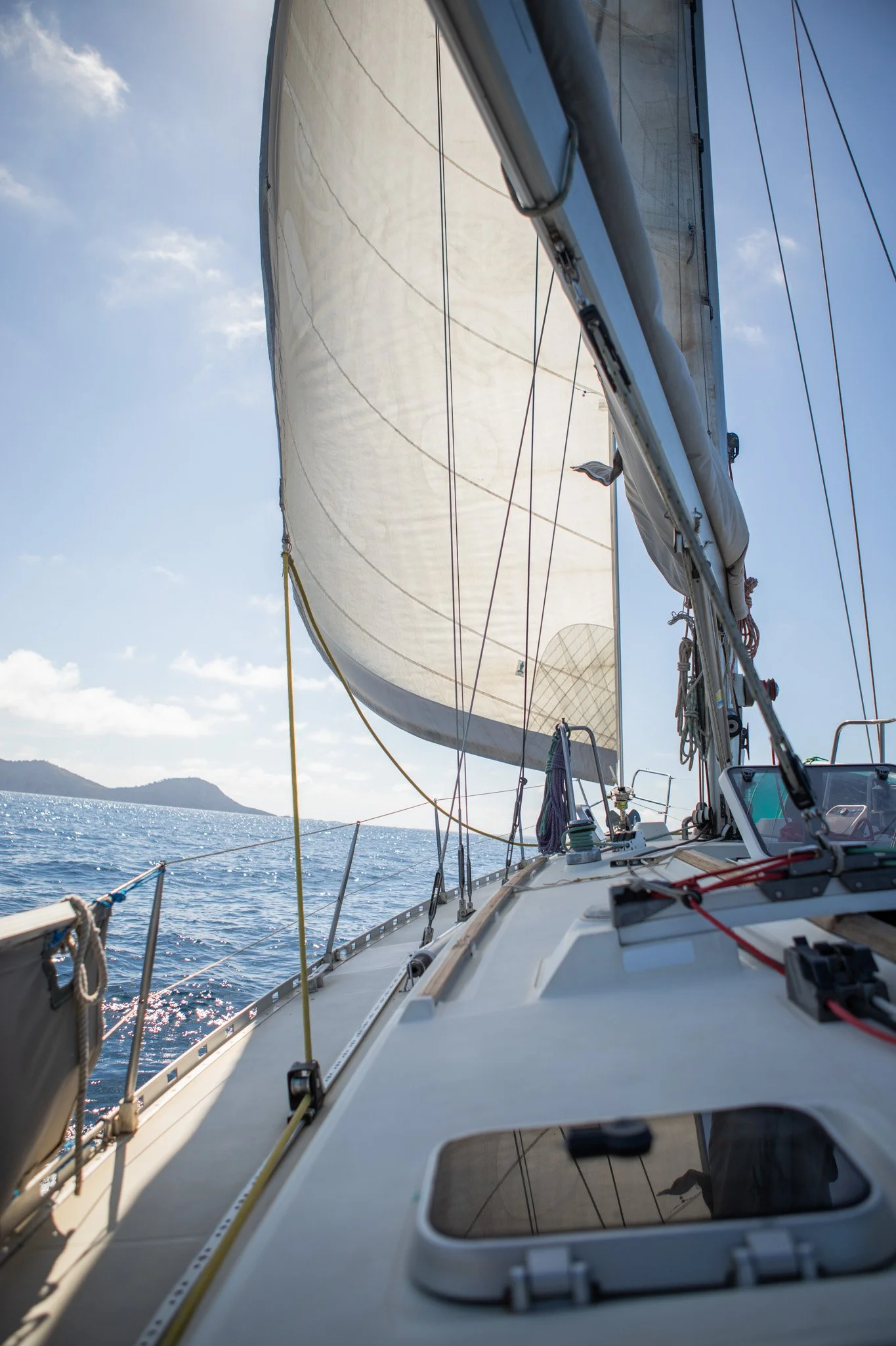 Vista desde el mástil de un velero en el mar, con velas desplegadas bajo un cielo parcialmente nublado.