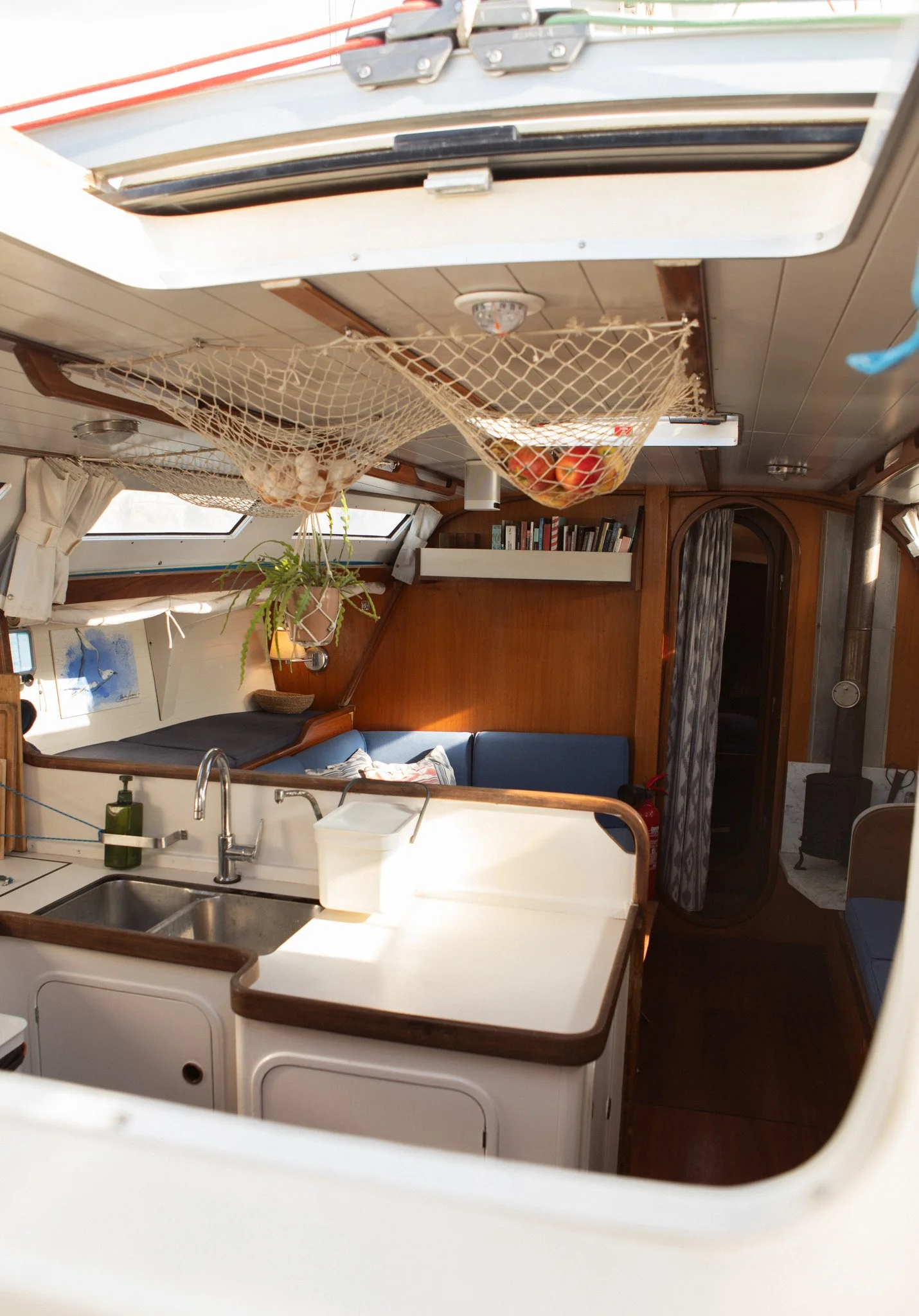 Interior de una cabina de barco con cocina, sala y biblioteca, con ventanas grandes y muebles de madera.