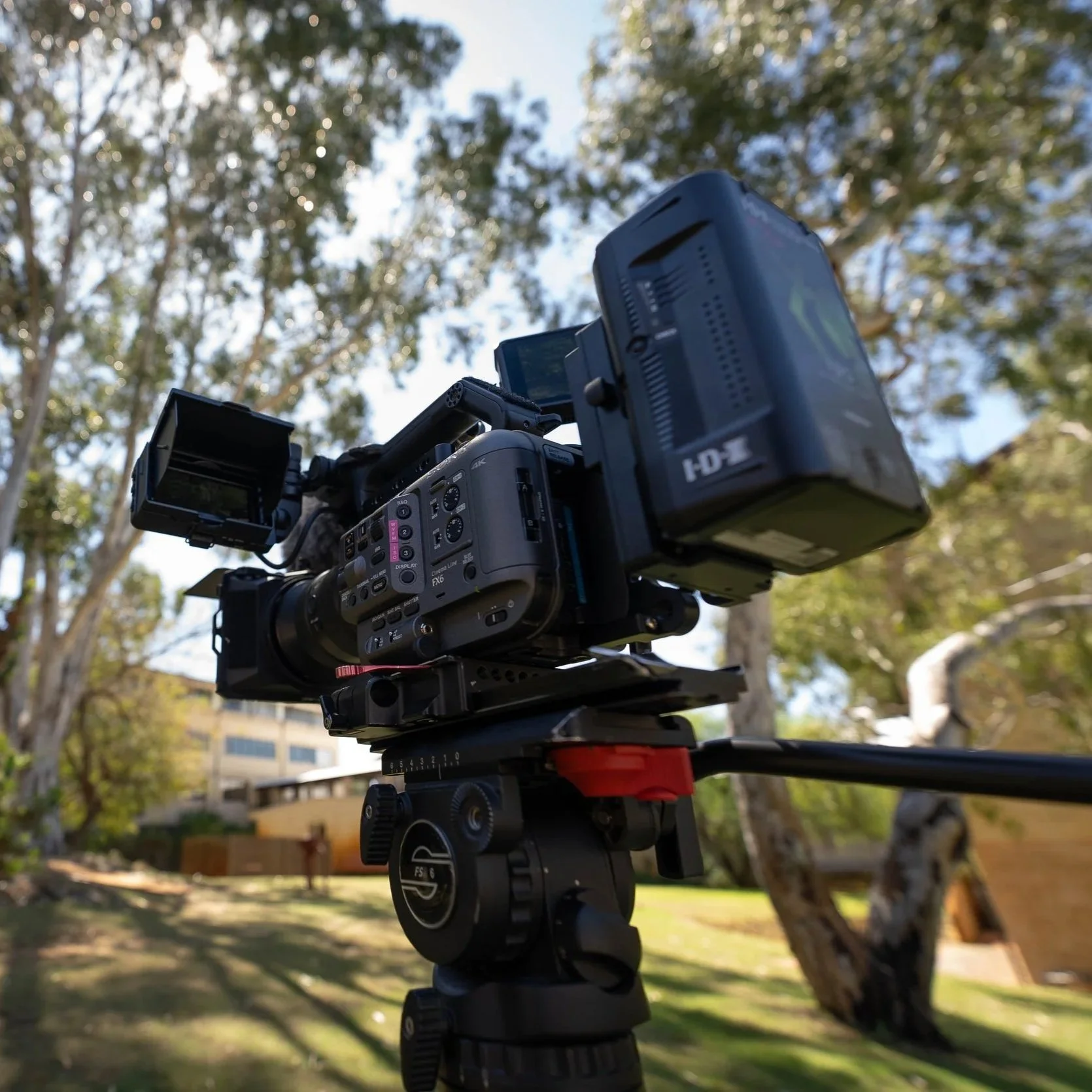 Camera mounted on a tripod outdoors, with trees and buildings in the background.