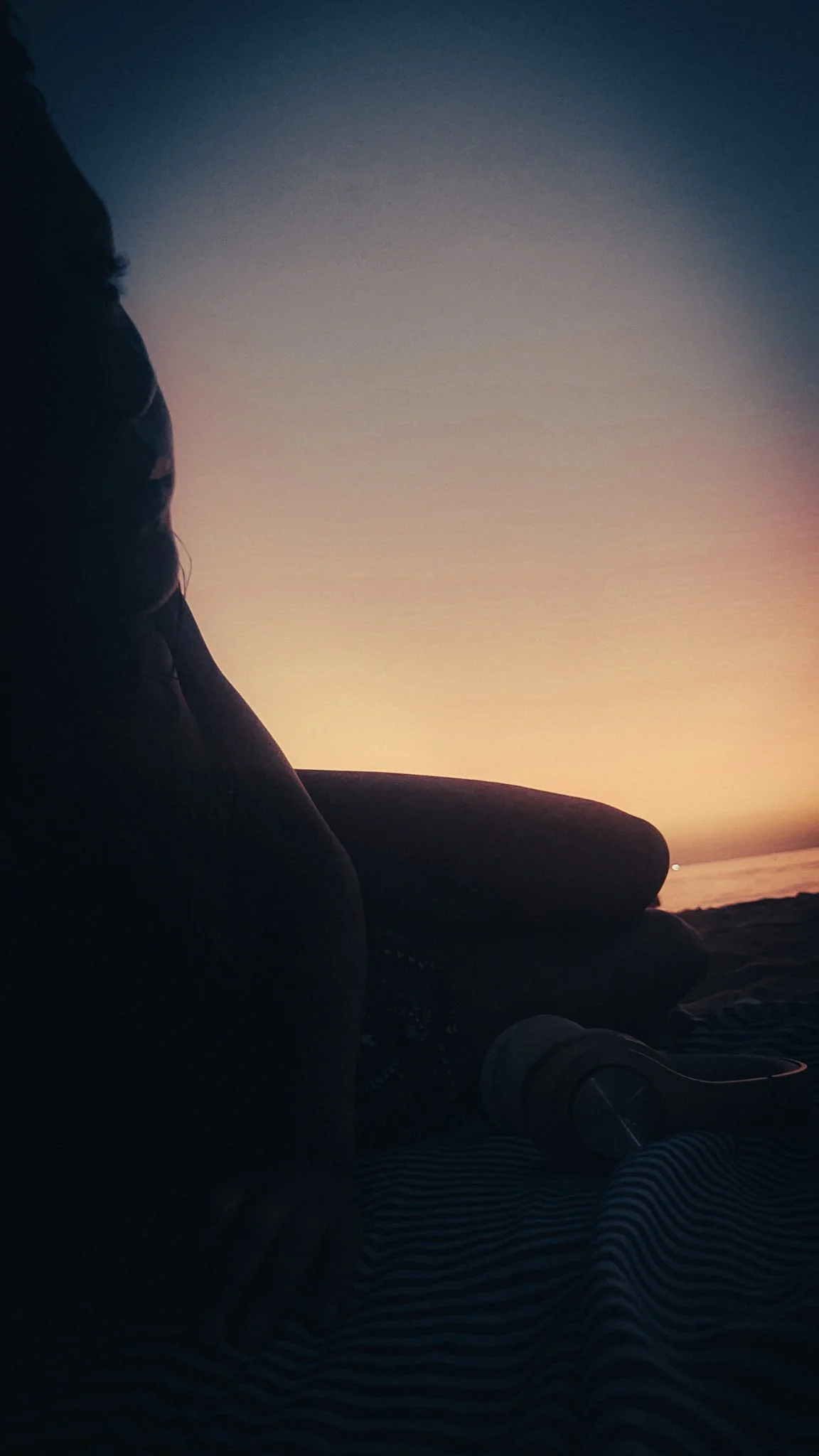 Woman sitting in silhouette on a beach at sunset in Thailand.