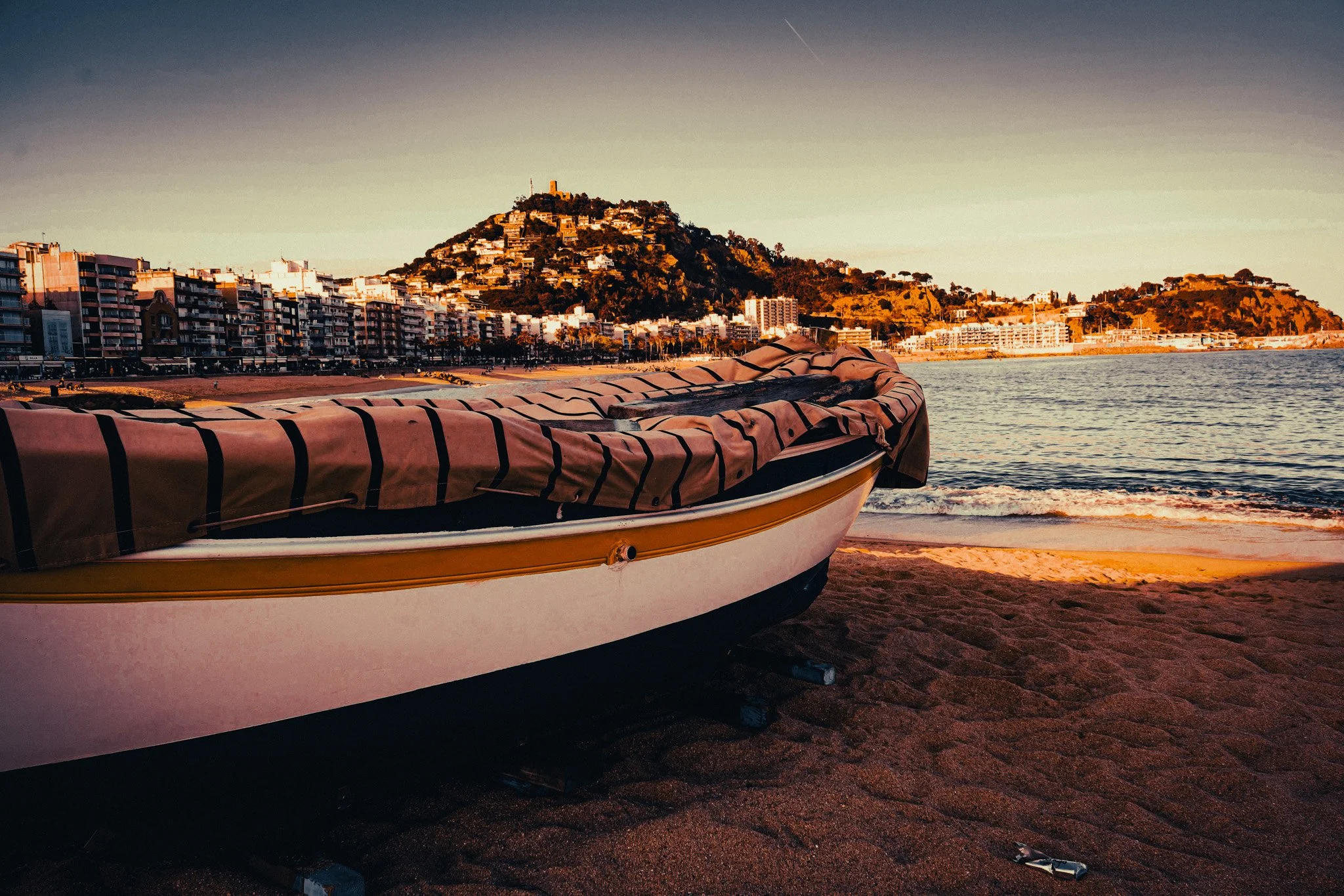Traditional boat on Lloret de Mar beach with the town and coastline behind it on the Costa Brava.