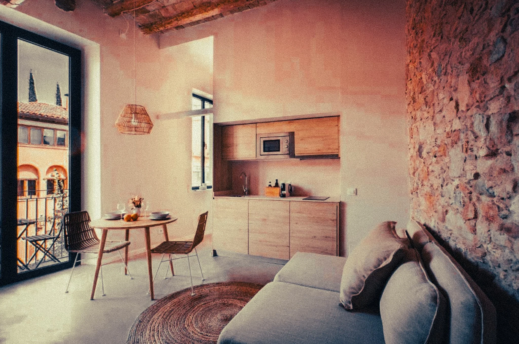 Modern open-concept kitchen and dining area with large sliding glass doors leading to a balcony, a round dining table with chairs, a kitchen with wooden cabinets, a microwave, and a textured brick wall, with a cozy seating area featuring a sofa and p