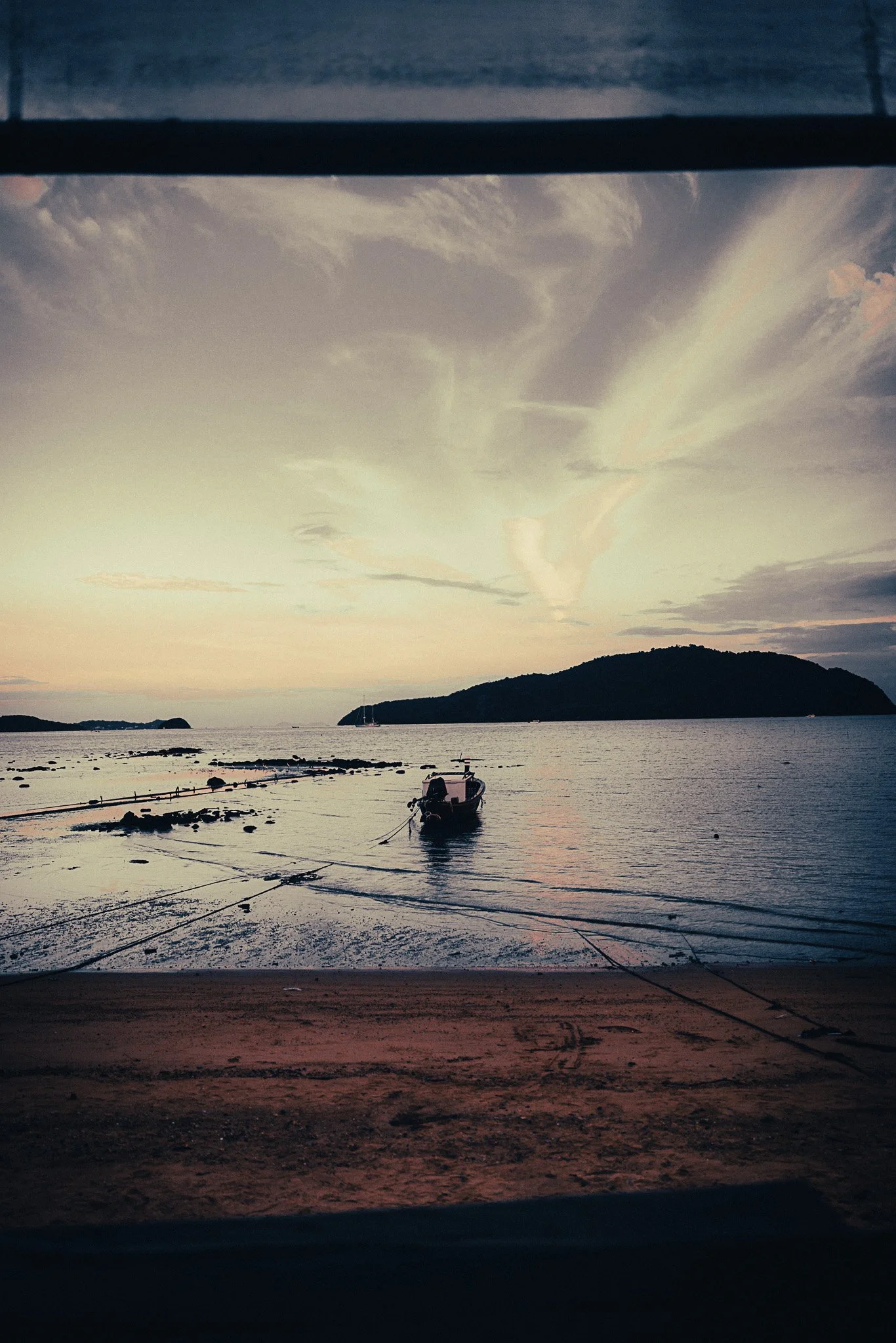 Sunset view over the sea in Phuket, Thailand, with a longtail boat at low tide.