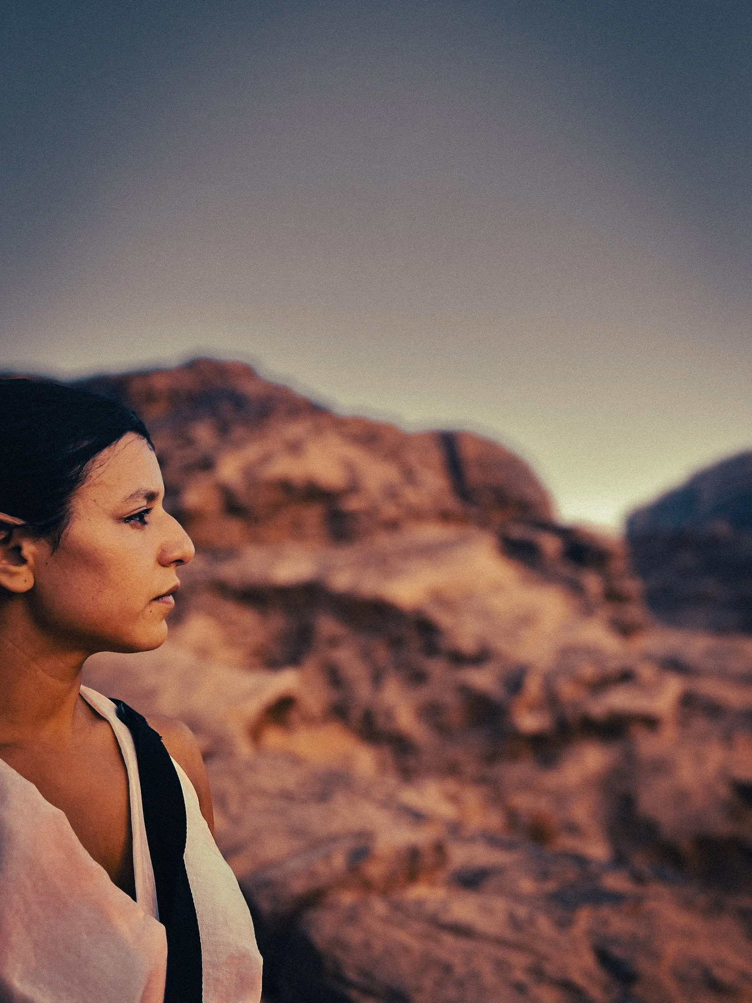 Woman in side profile standing in Wadi Rum desert, with warm red sandstone mountains blurred in the background.
