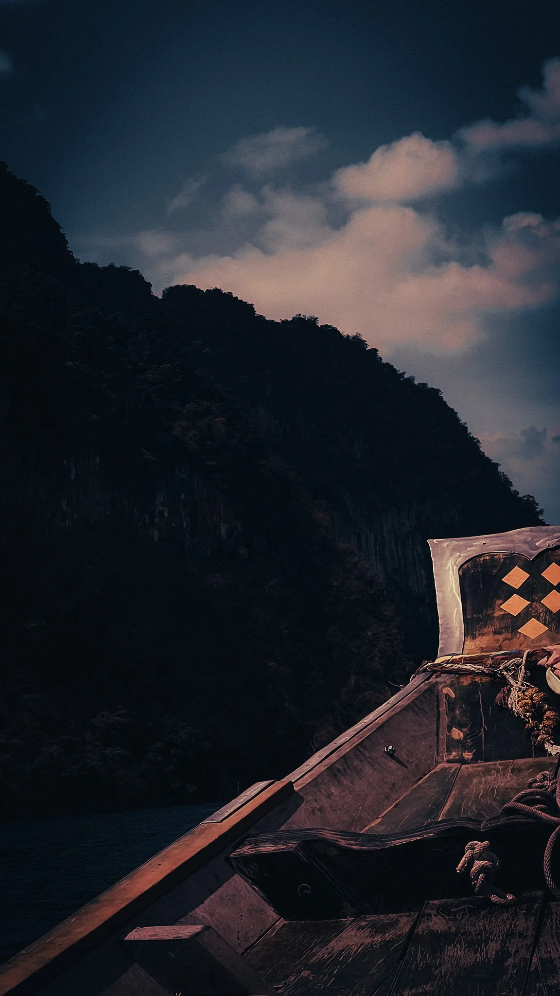 Longtail boat on Cheow Lan Lake in Khao Sok, Thailand, passing dark limestone cliffs and turquoise water under a blue sky.