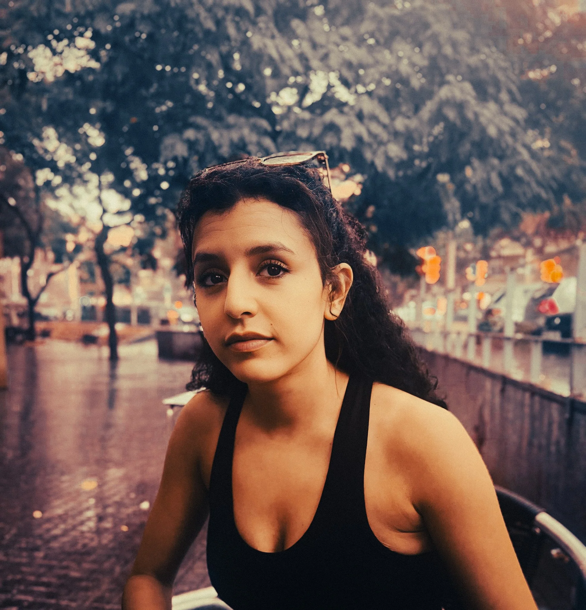 Woman sitting by the water in Barcelona on a rainy day, with soft retro tones and blurred city trees in the background.