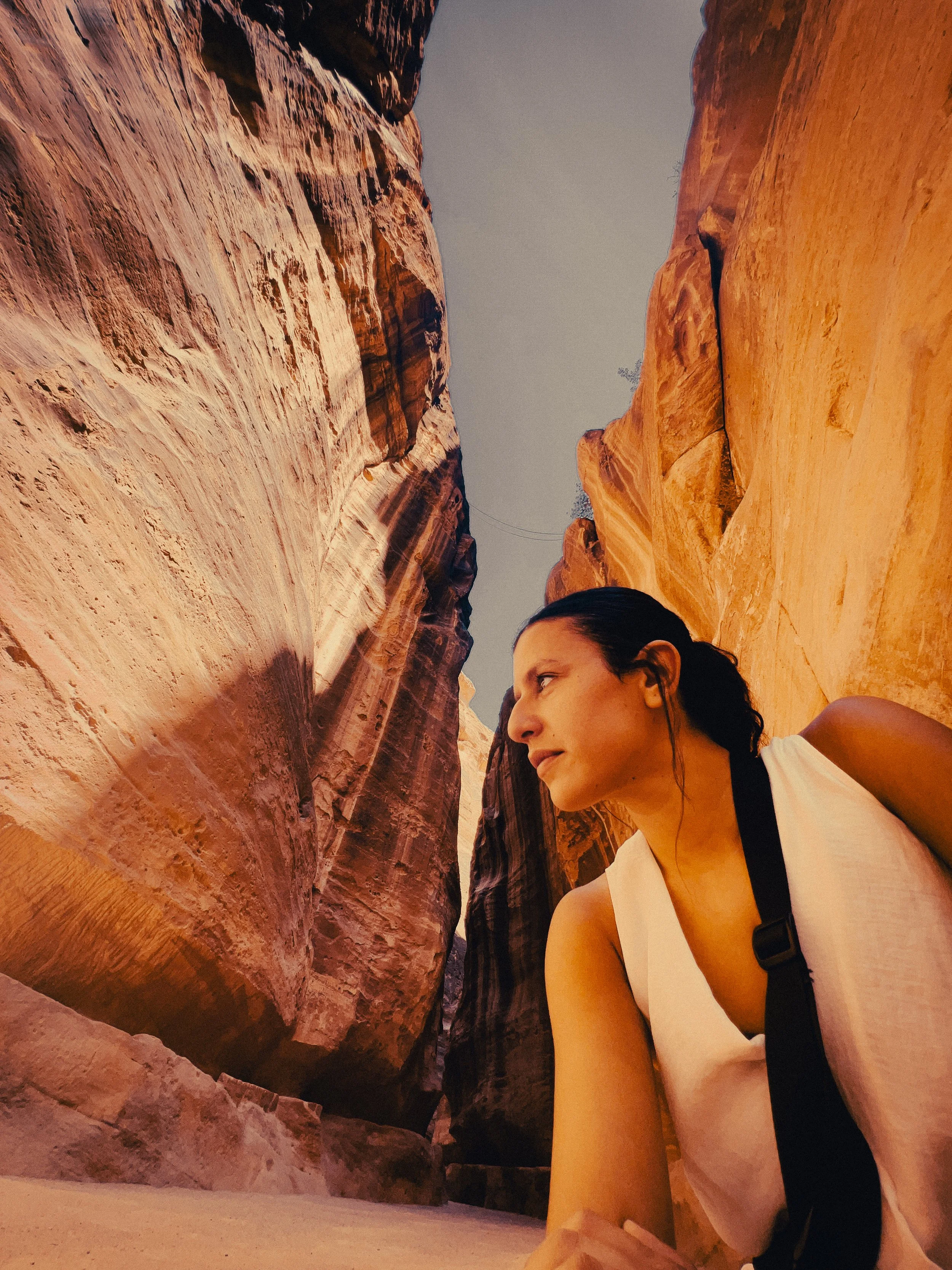 Woman in a white sleeveless outfit walking through the narrow sandstone canyon at Petra, Jordan.