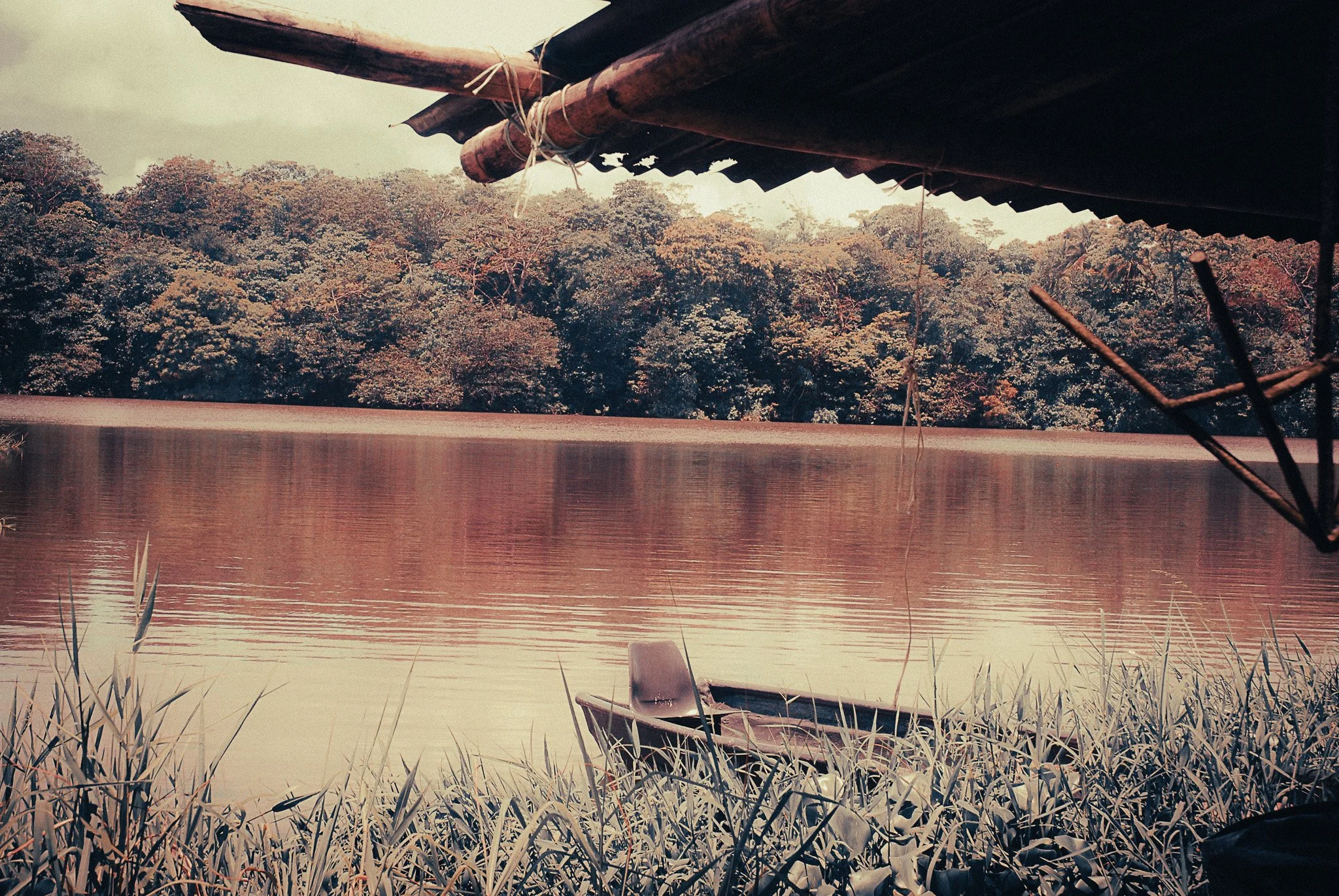 Small motorboat moored beside a jungle river in Parismina, Costa Rica, beneath a rustic wooden shelter.