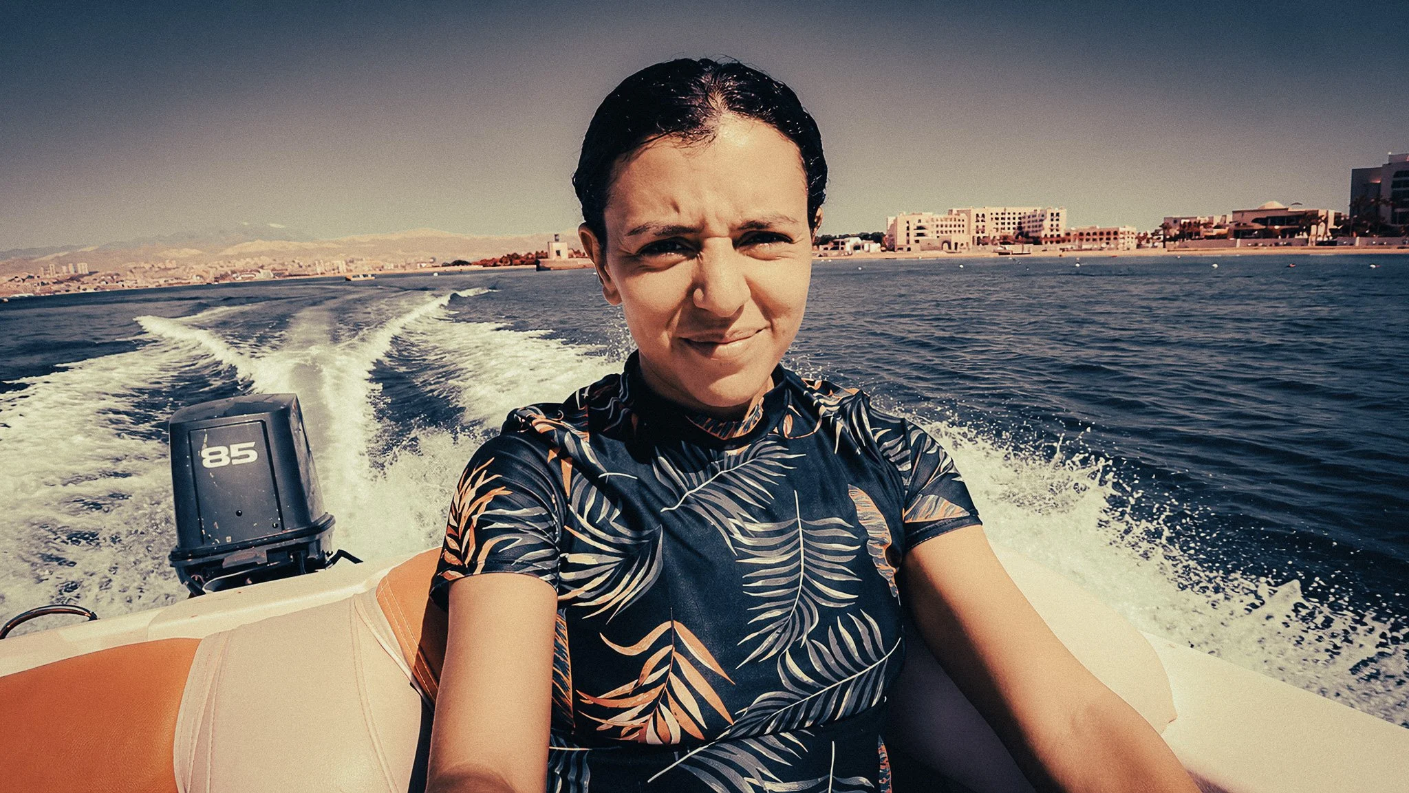 Solo female traveller on a boat in Aqaba, Jordan, with blue sea, white boat wake, and coastal mountains in the background.