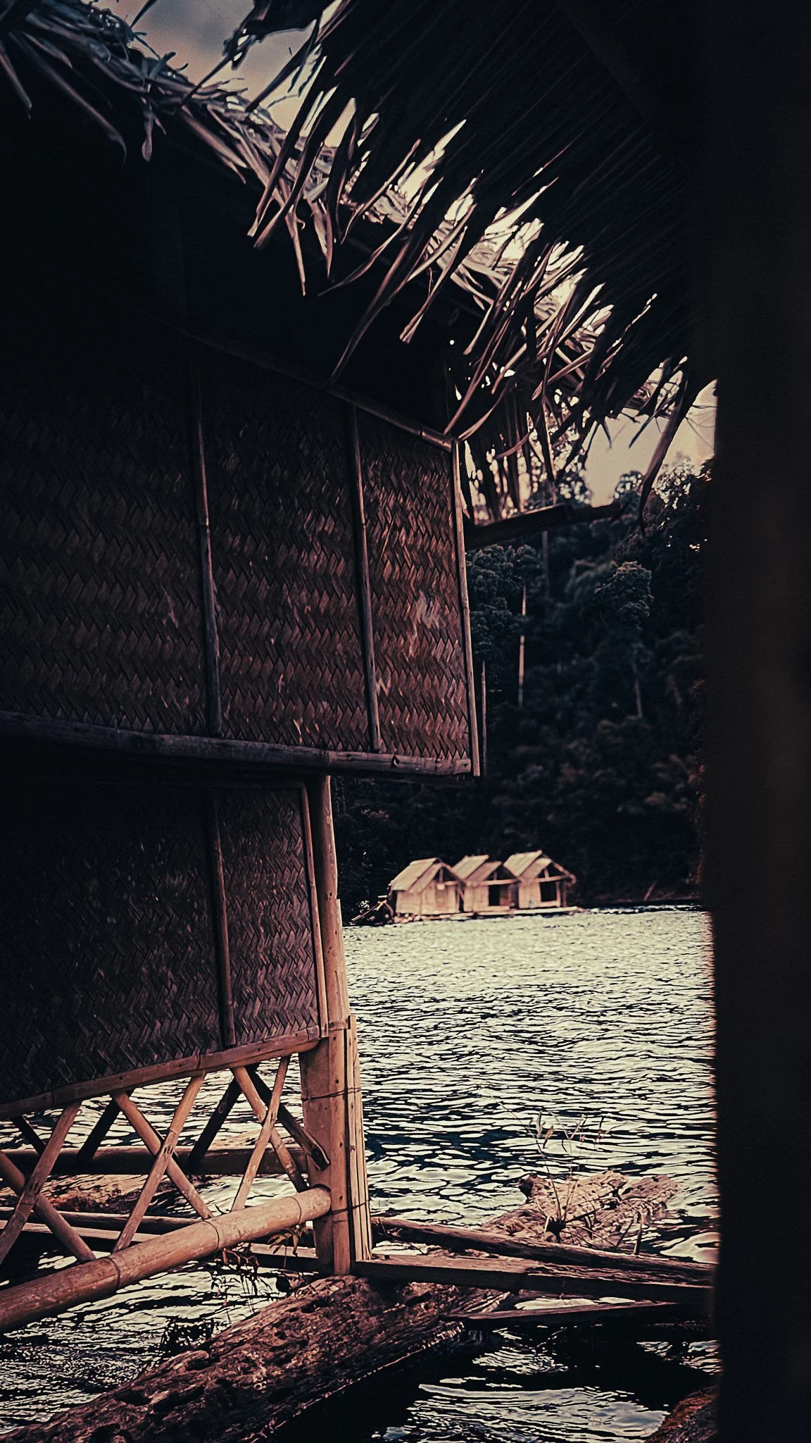 Bamboo floating bungalow on Cheow Lan Lake in Khao Sok, Thailand, with forested cliffs and more floating huts across the water.