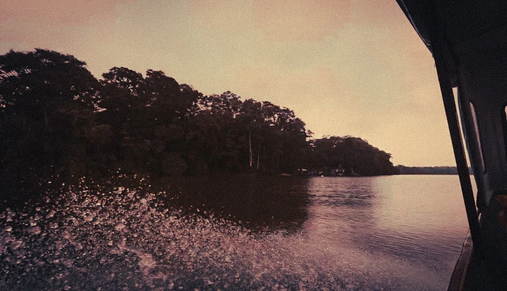 View from a boat travelling through Costa Rica’s Caribbean canals between Parismina and Moín on the route toward Puerto Viejo, with jungle trees lining the water at sunset.