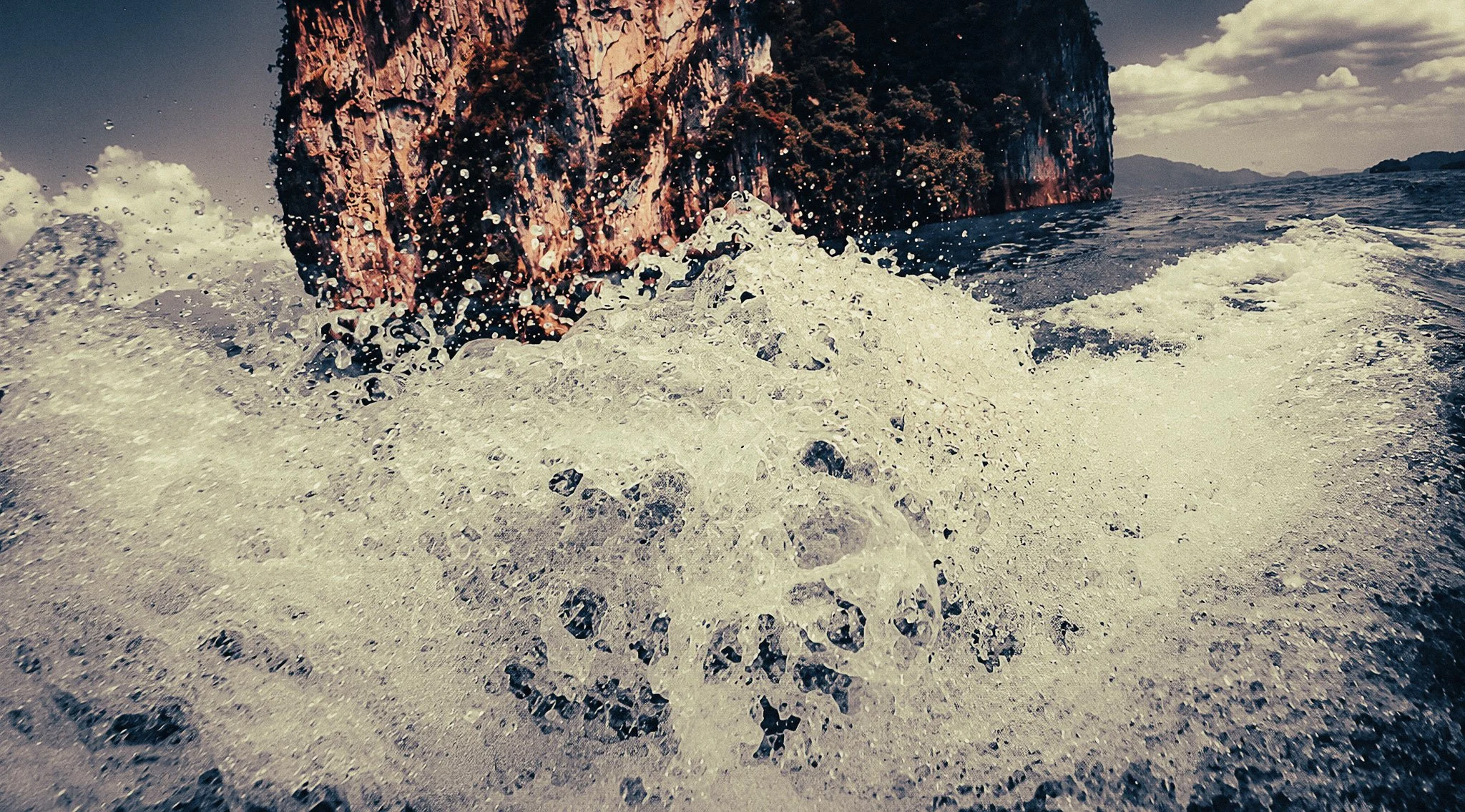 Longtail boat wake splashing beside limestone cliffs on Cheow Lan Lake in Khao Sok, Thailand.