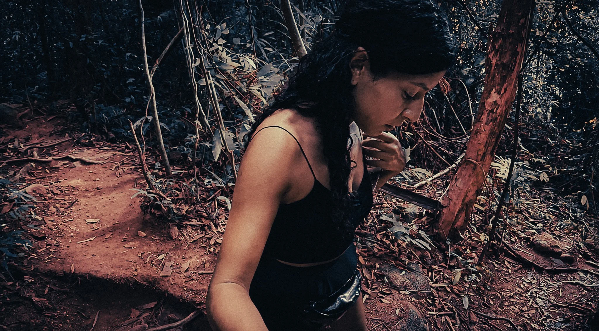 Solo female traveller hiking through the rainforest in Khao Sok, Thailand, walking along a dirt jungle trail surrounded by roots, trees and dense green plants.