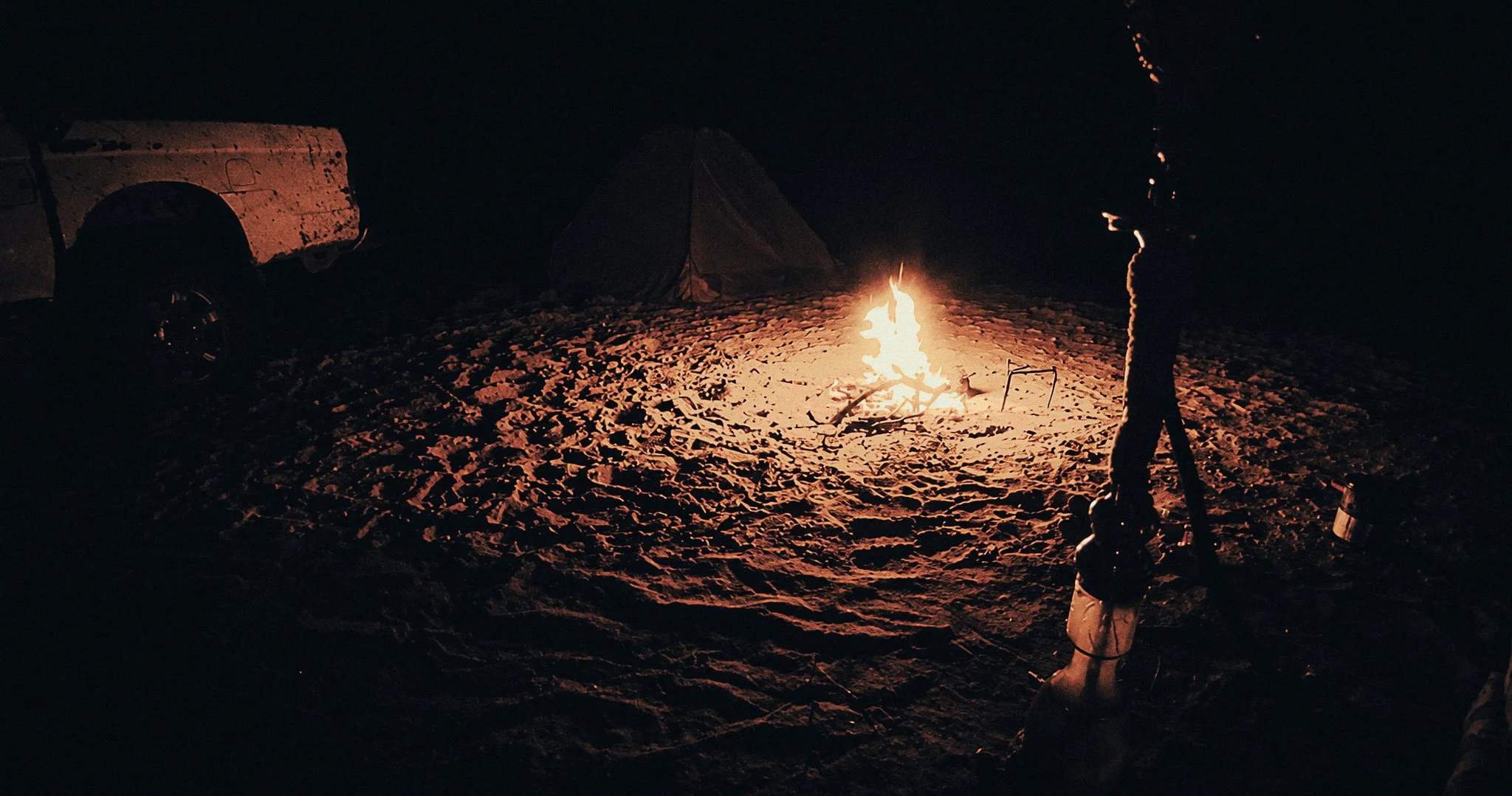 Campfire burning beside a small tent and parked jeep during an overnight stay in the Wadi Rum desert.