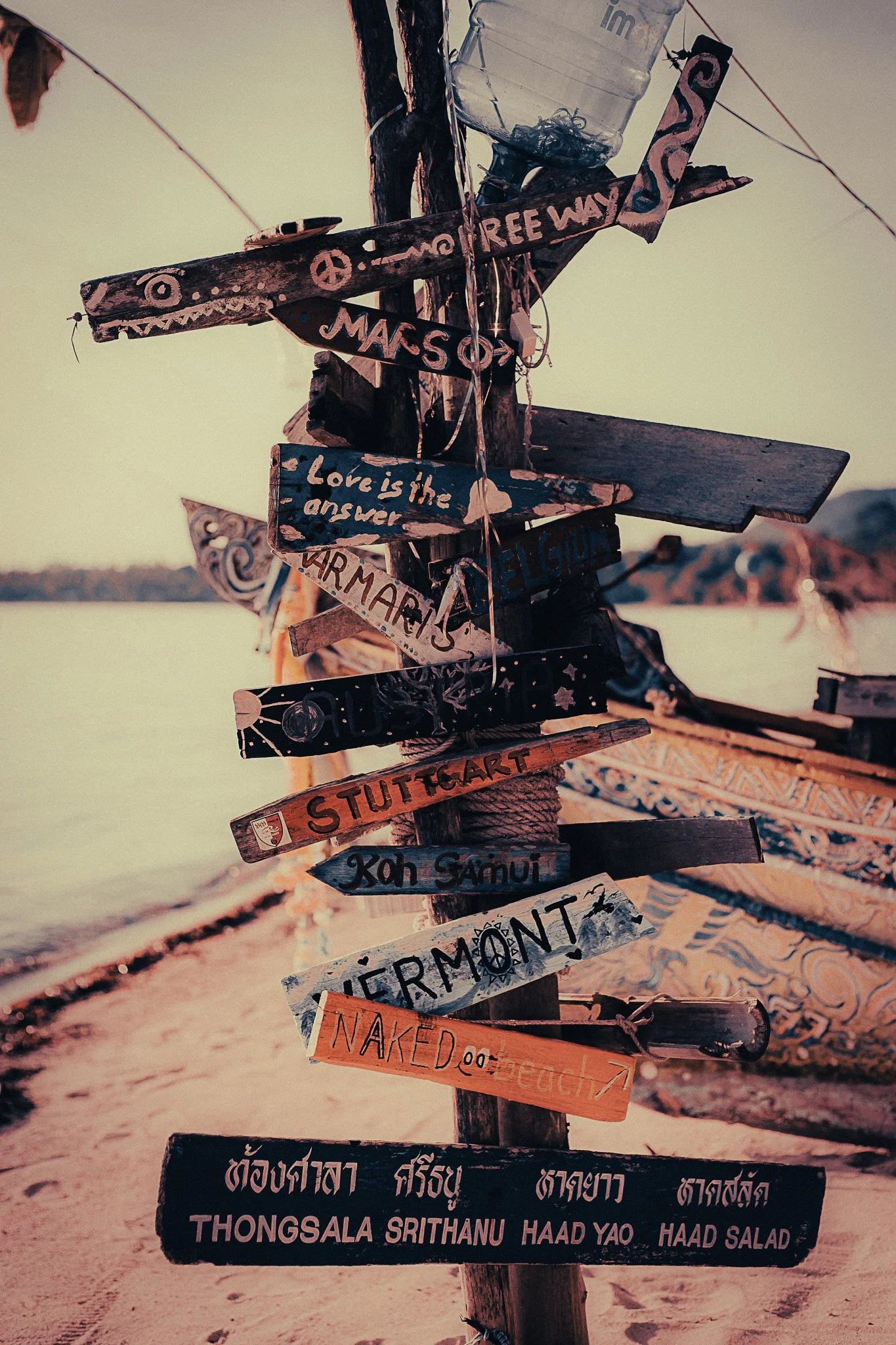 Hand-painted wooden signs on a beach in Thailand with traditional boats in the background.