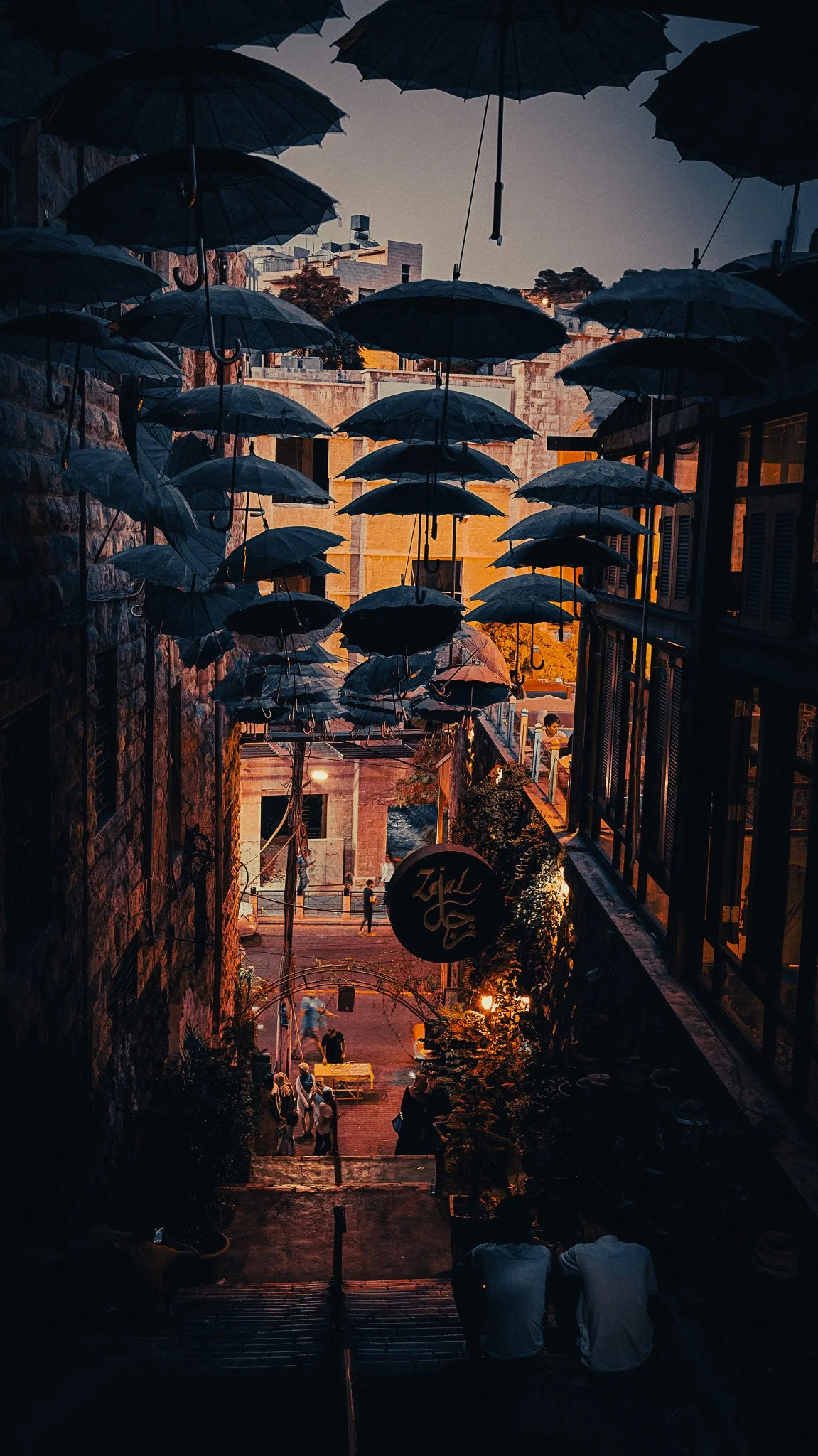 Narrow downtown Amman street at night, decorated with hanging umbrellas and warm lights between old stone buildings.