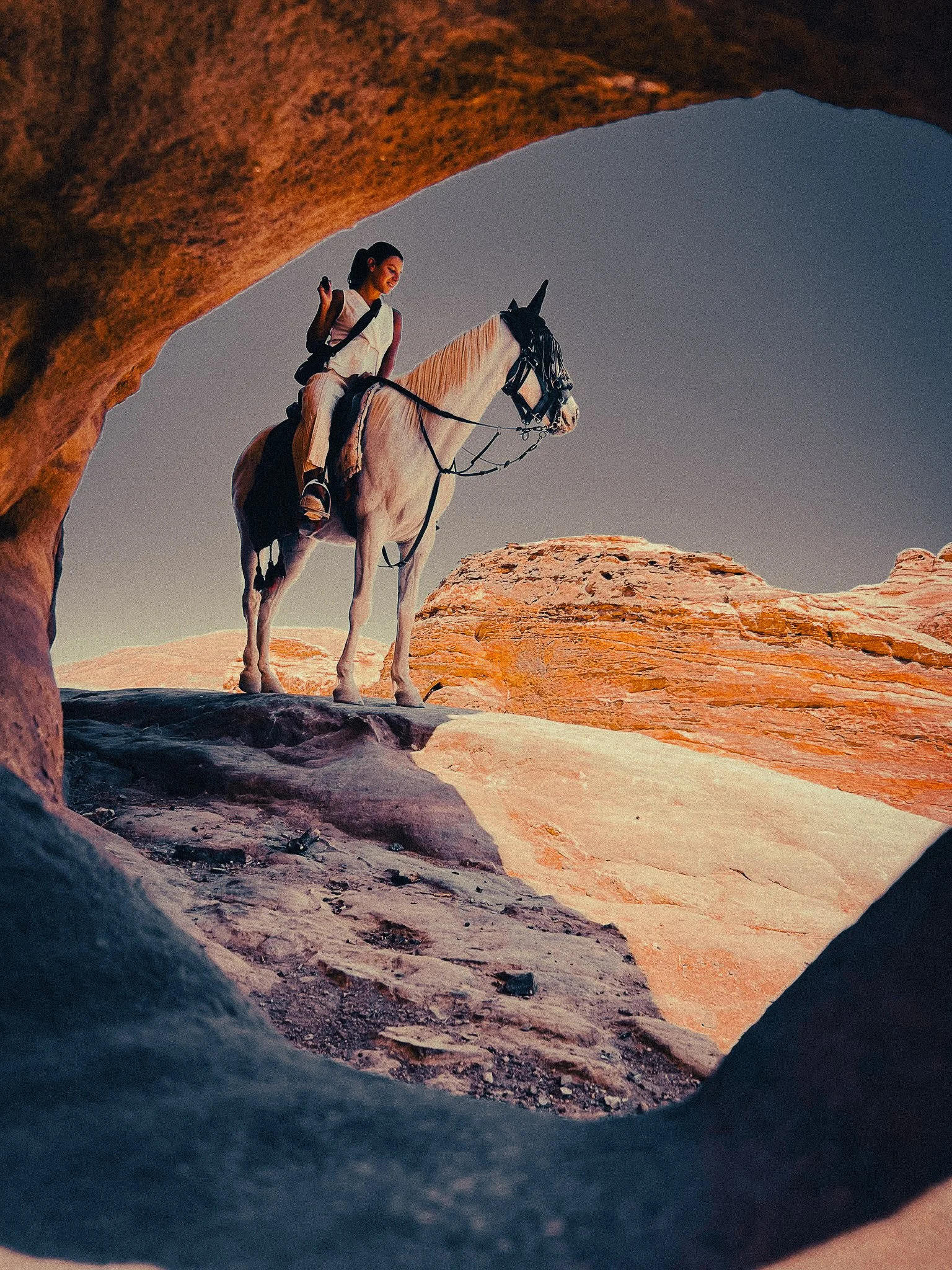 Woman riding a white horse beneath a sandstone arch in Petra, Jordan.