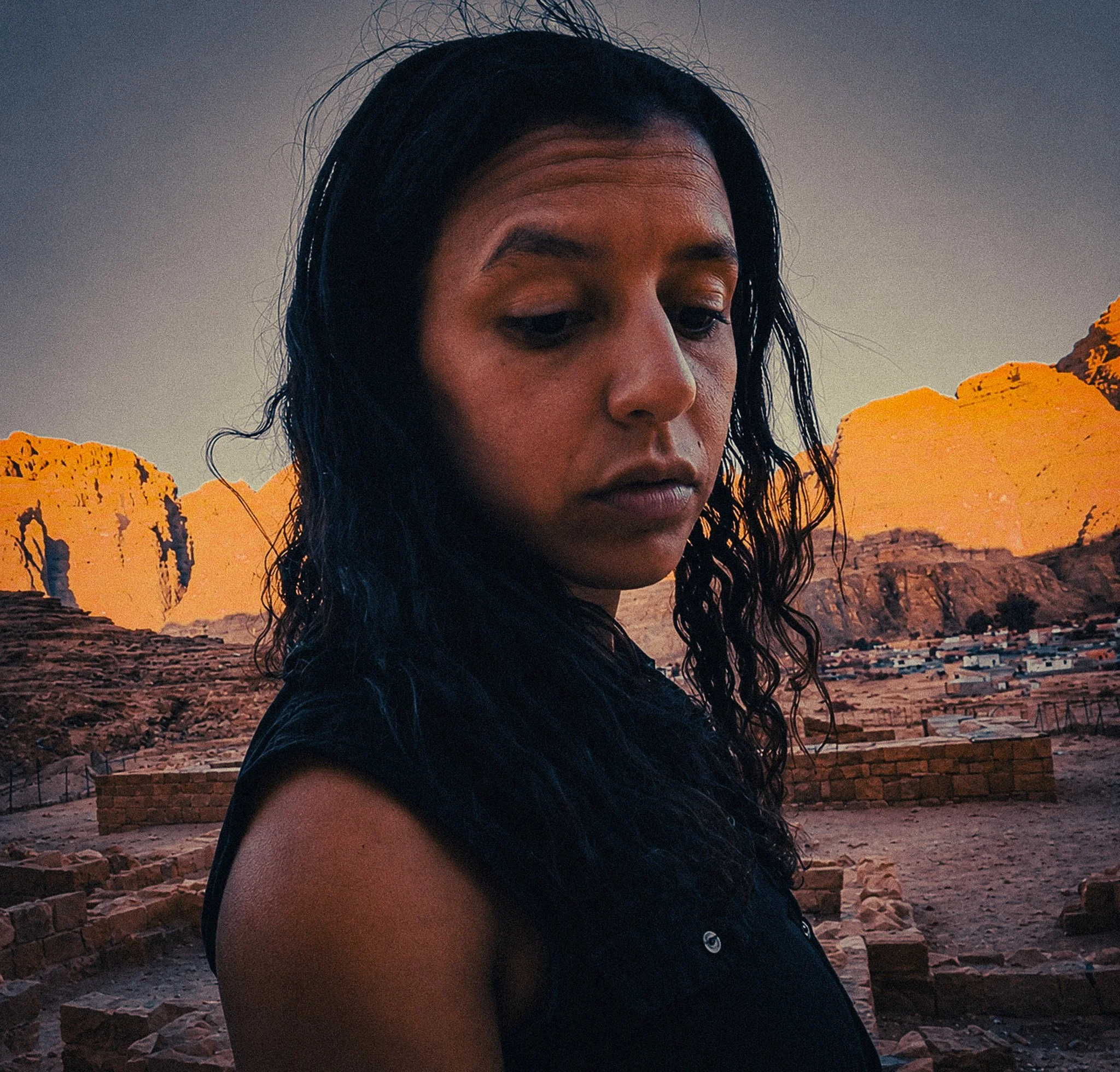Woman standing in Wadi Rum Village at golden hour, with desert mountains, stone ruins and warm evening light behind her.