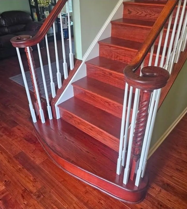 Wood staircase with white spindles and dark wooden handrails, next to a curved wood floor landing.