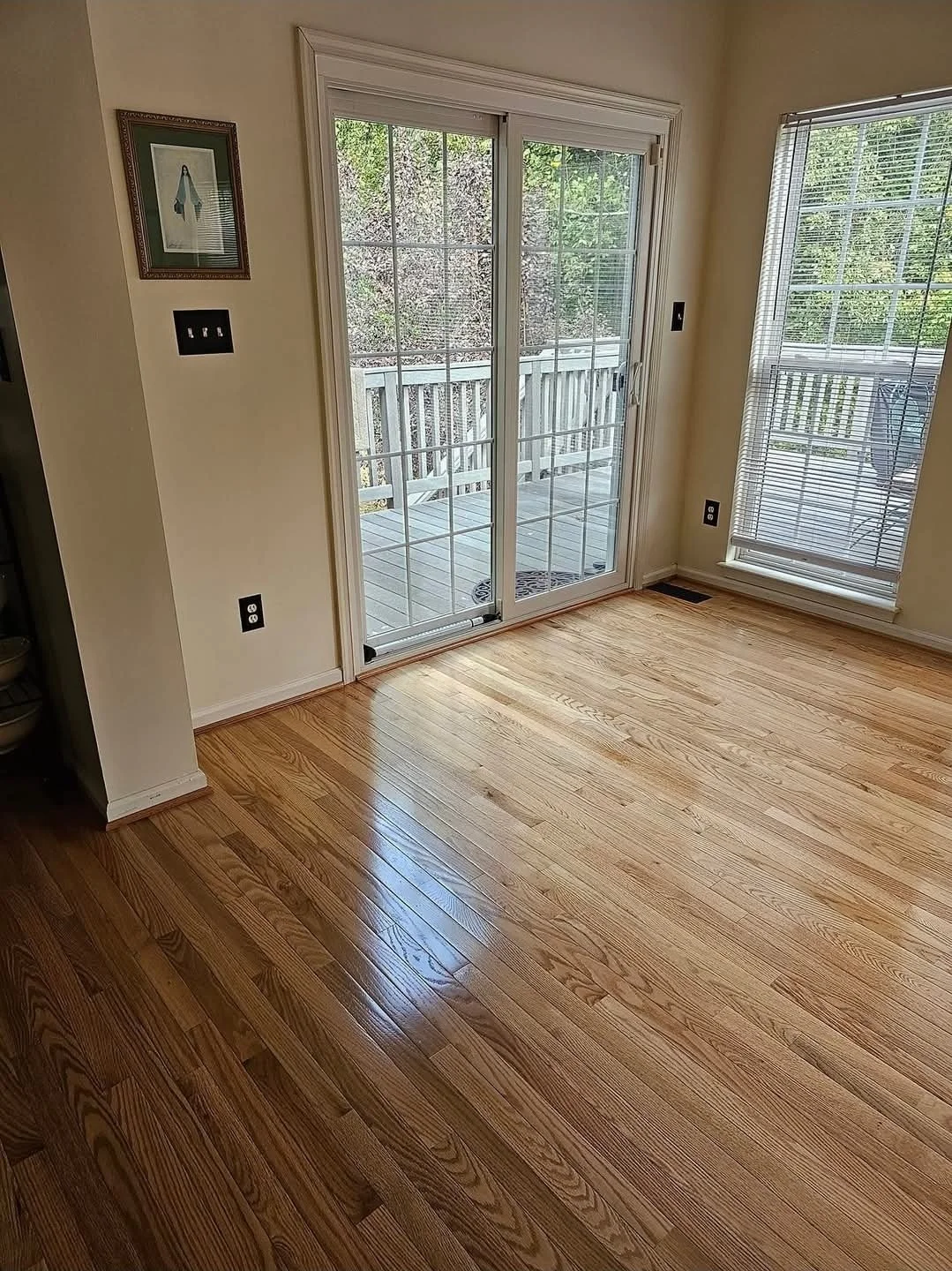Empty room with wooden flooring, sliding glass door to a deck, and a window with blinds.
