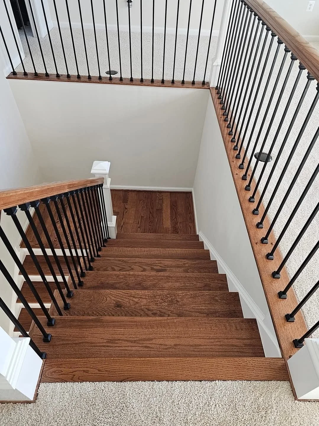 Top-down view of wooden staircase with black metal baluster.