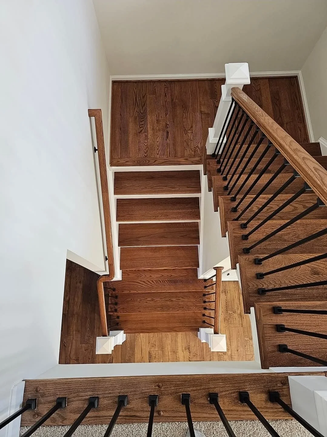 View looking down a staircase with wooden steps and black metal balusters, showing the landing and upper floor with matching wooden flooring.