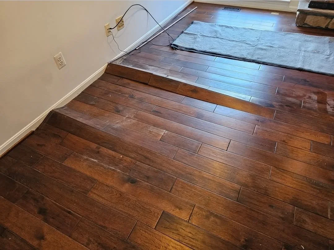 Refinished hardwood floor with a transition strip and a small rug near the window.