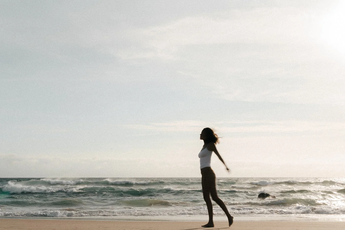 A woman walking along the beach with the ocean and sky in the background during sunset.