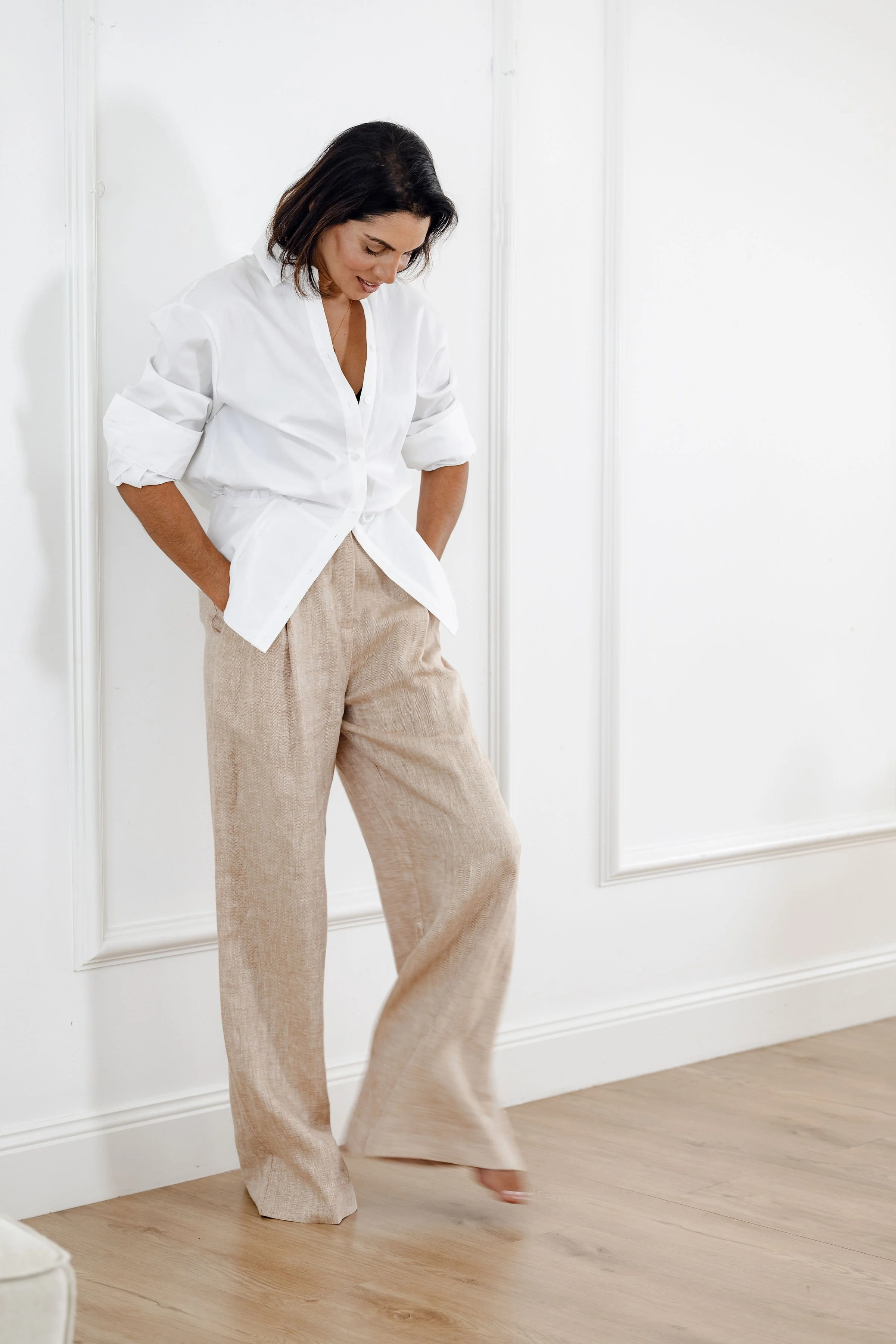 Woman wearing a white shirt and beige wide-leg pants standing against a white wall.