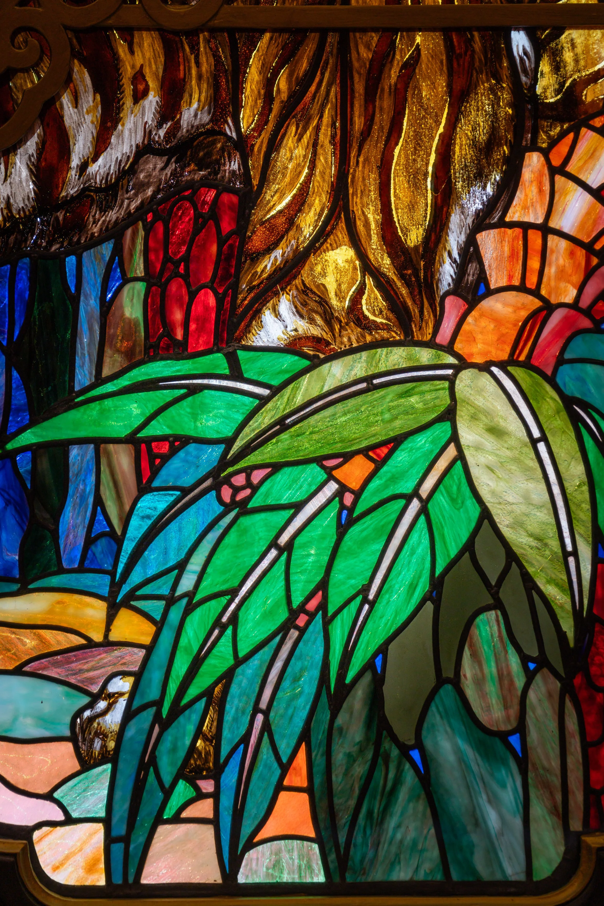 Close-up of a colorful stained glass window featuring abstract shapes with shades of green, blue, orange, red, and yellow, outlined by black lead lines.