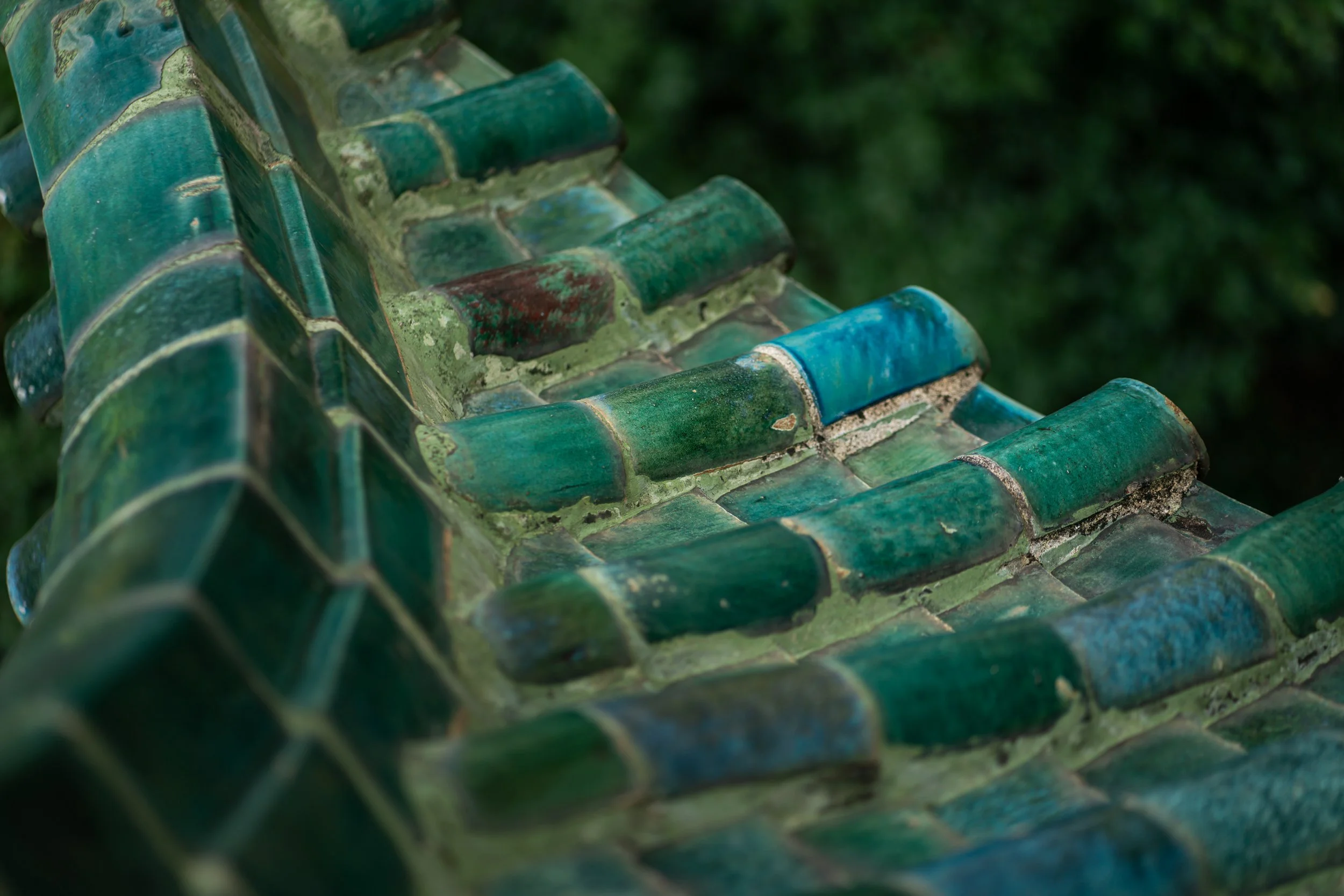 Close-up of a traditional Asian-style ceramic roof with green glazed tiles, showing weathering and moss growth.
