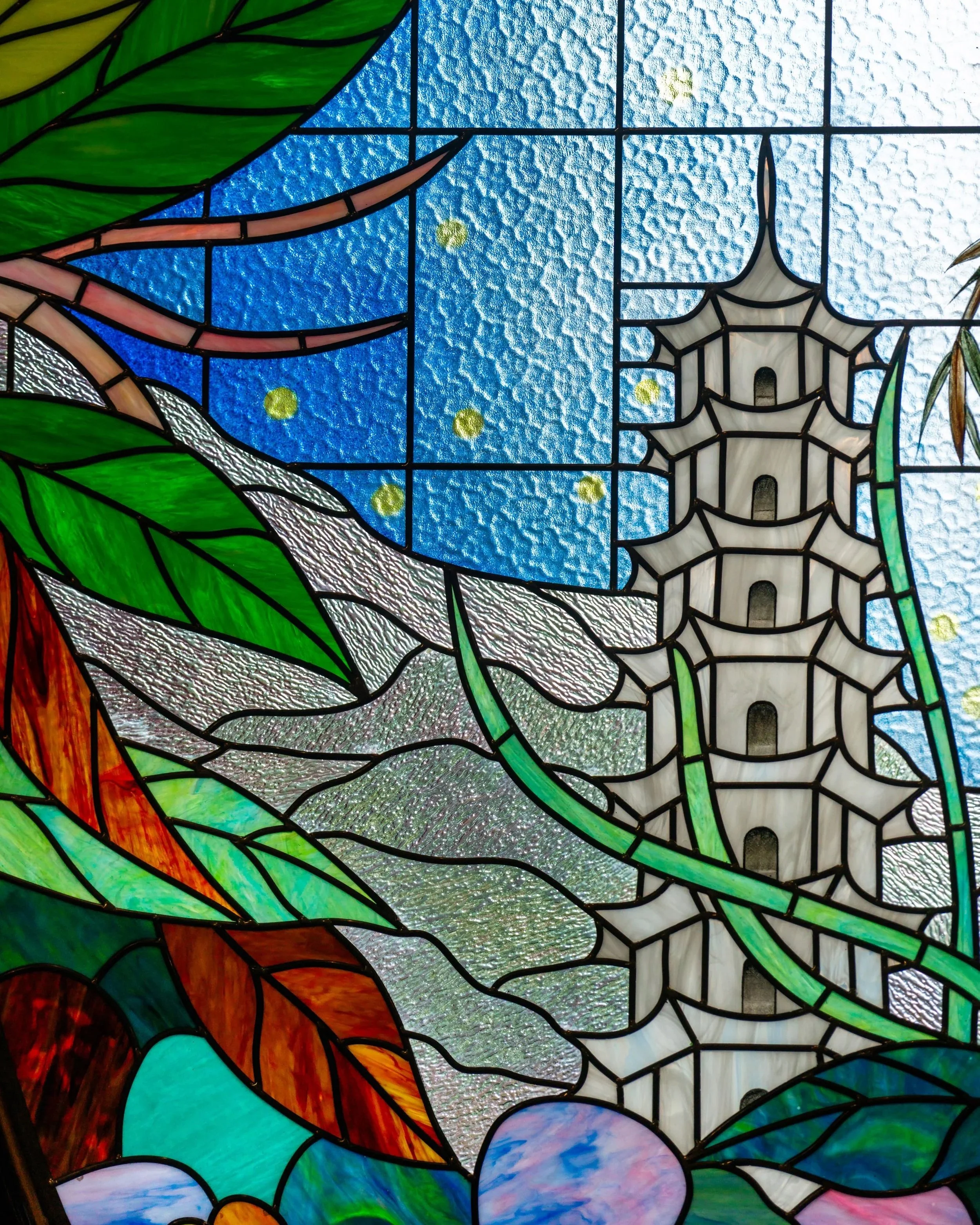 Colorful stained glass window featuring a pagoda-style building and natural landscape elements.