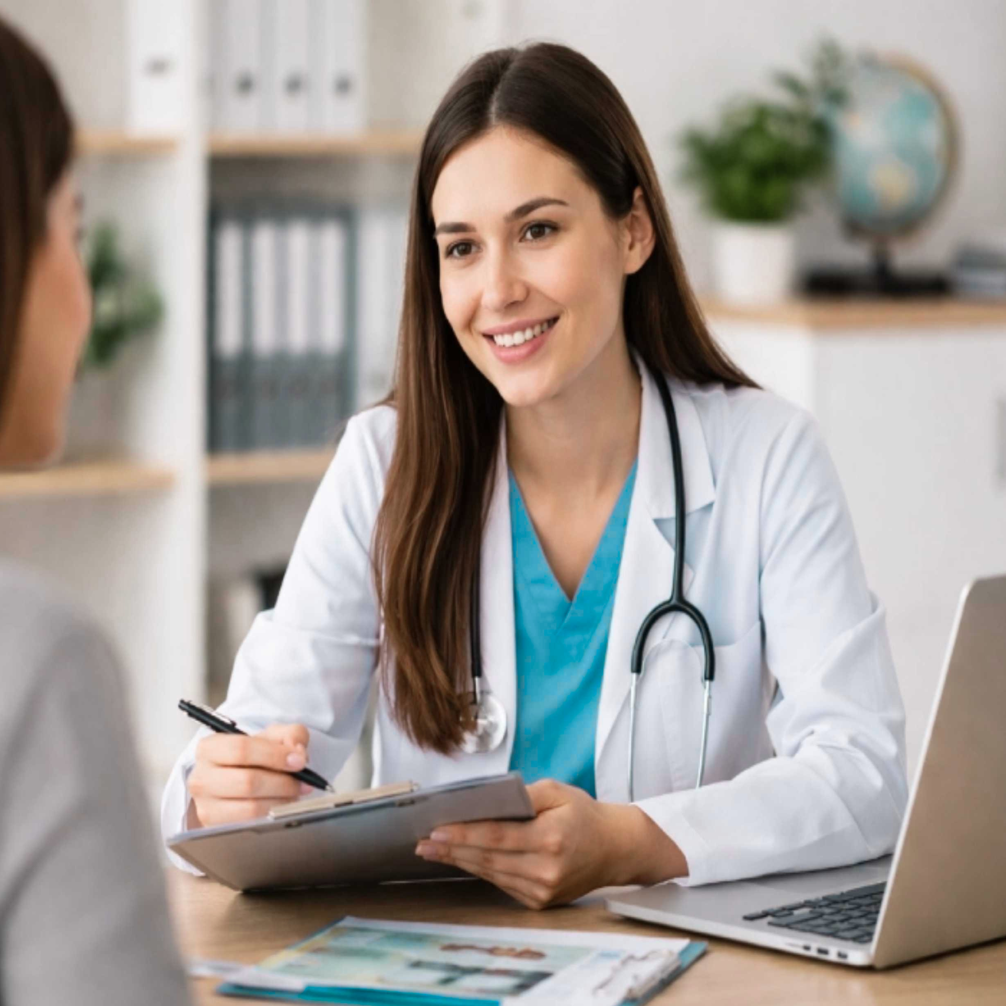 A medical professional speaking with a patient in an office, holding a clipboard and smiling.