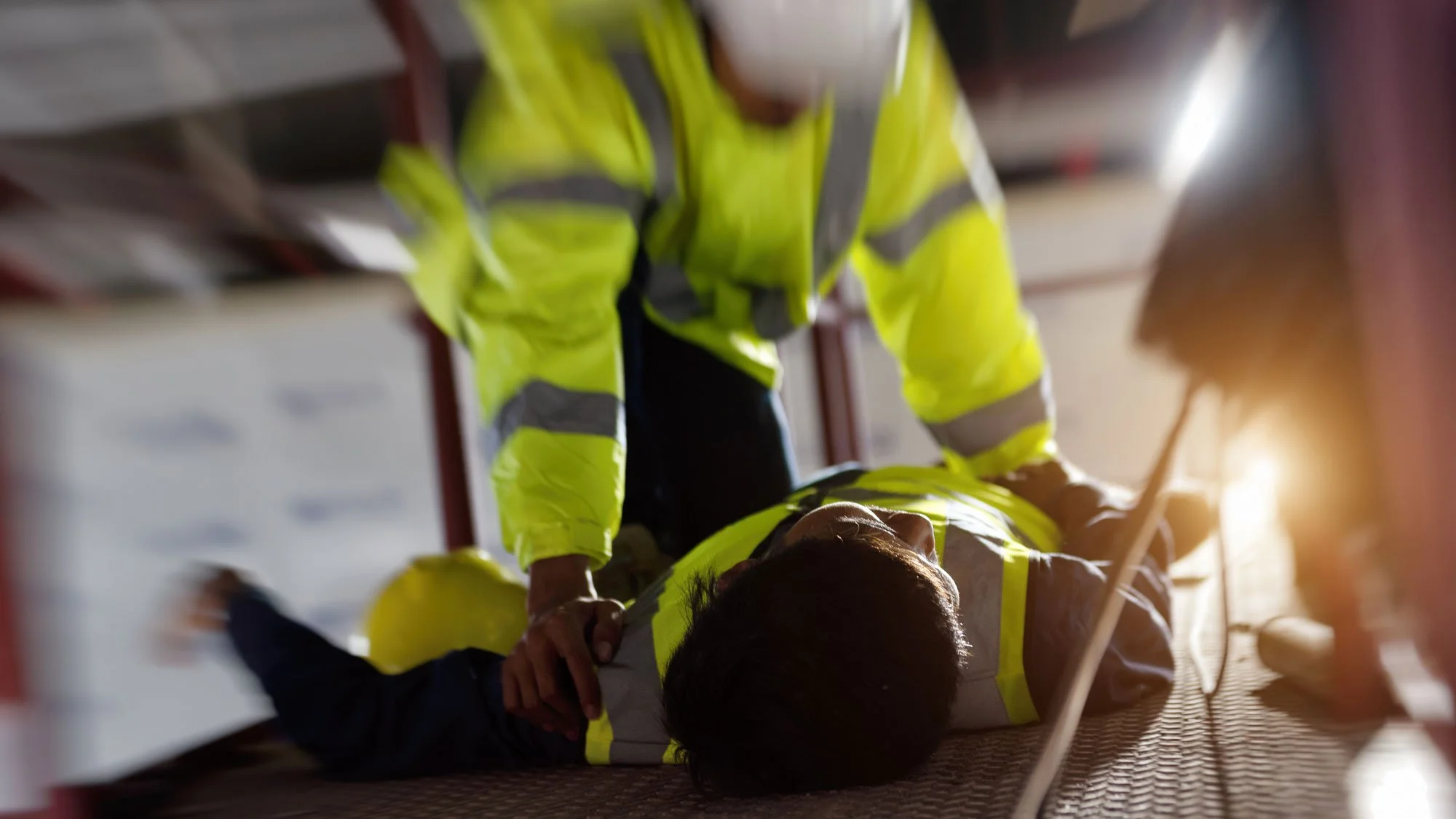 Two workers in high-visibility safety jackets assisting an injured person lying on a metal stretcher during an emergency response.