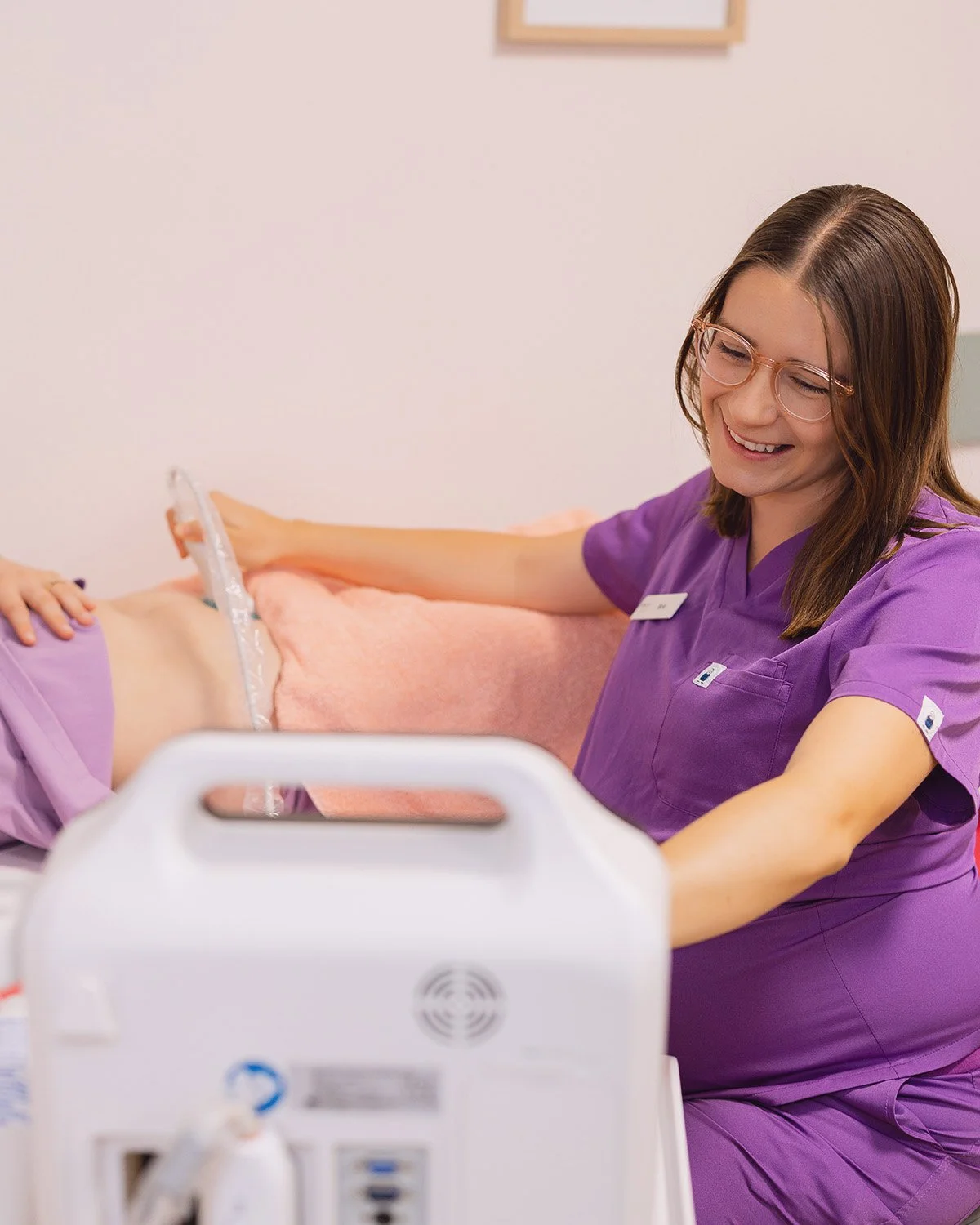 A healthcare professional in purple scrubs taking care of a patient in a hospital bed.