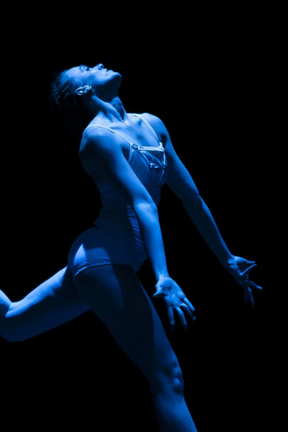 A dancer performs on stage, illuminated by blue lighting, with a dark background.