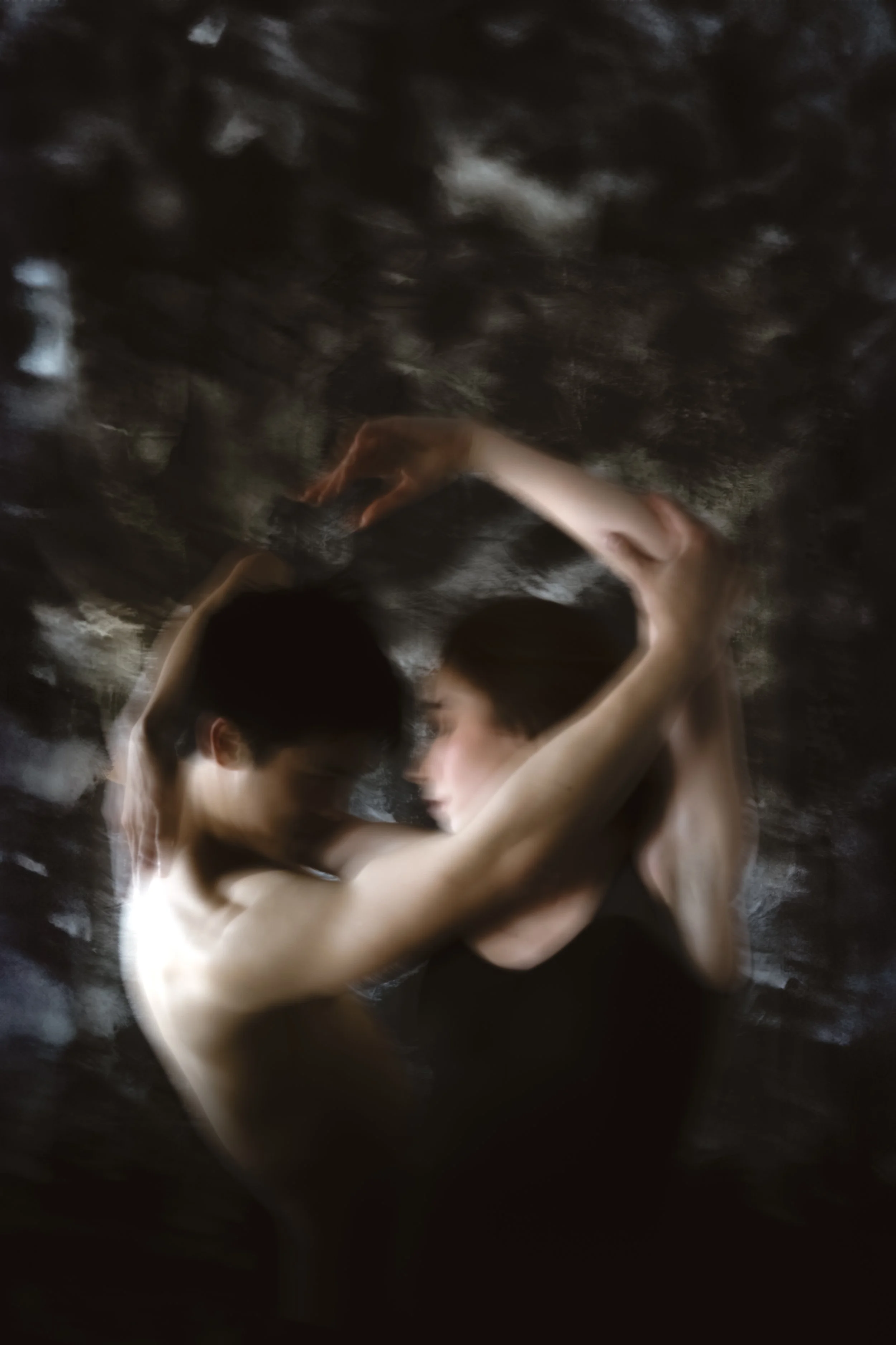 Two people lying close together with arms around each other, partially submerged in water, faces close, in a dark, reflective environment.