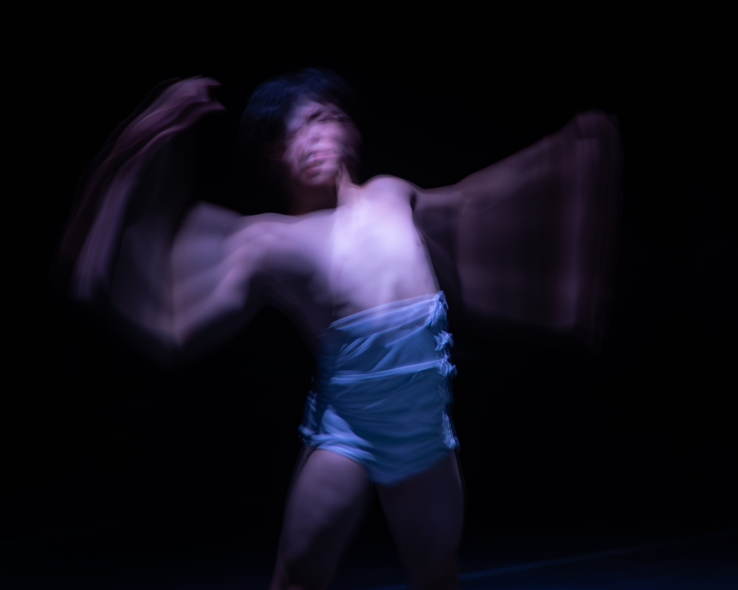 A person with short dark hair in motion, with a blurred effect, wearing light blue shorts, against a black background.