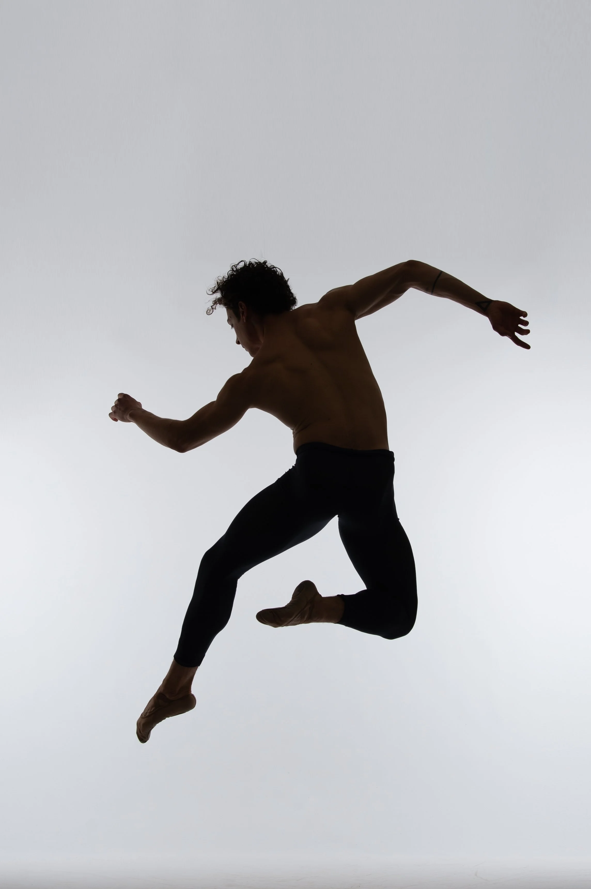 Silhouette of a male dancer mid-air against a gray background.