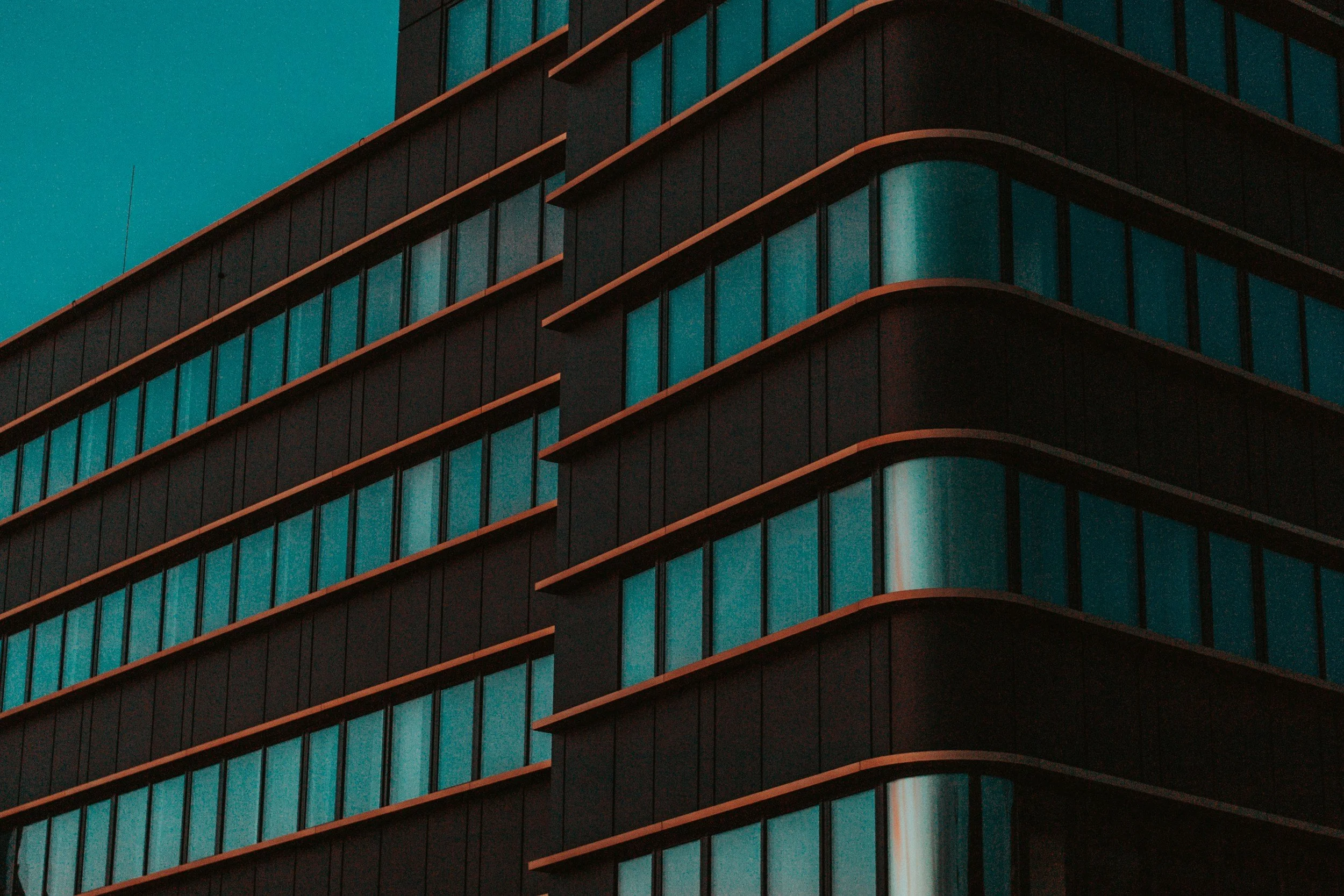 Close-up of a modern high-rise building with uniform rows of tinted windows and curved edges, highlighting architectural details at dusk.