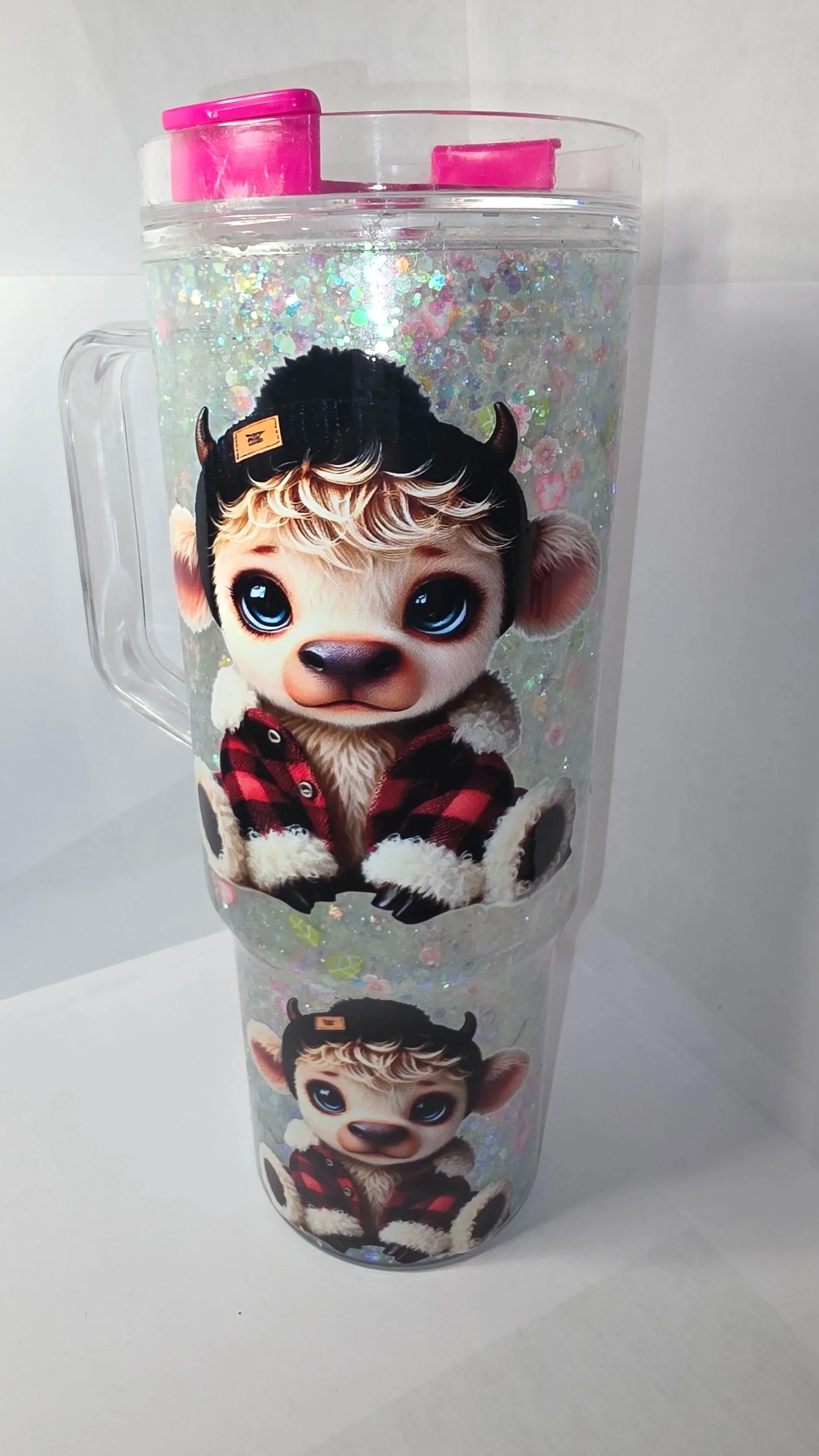 Two transparent tumblers with glitter and a cartoon character of a cute baby cow with large blue eyes, wearing a red and black plaid jacket, on a white background.