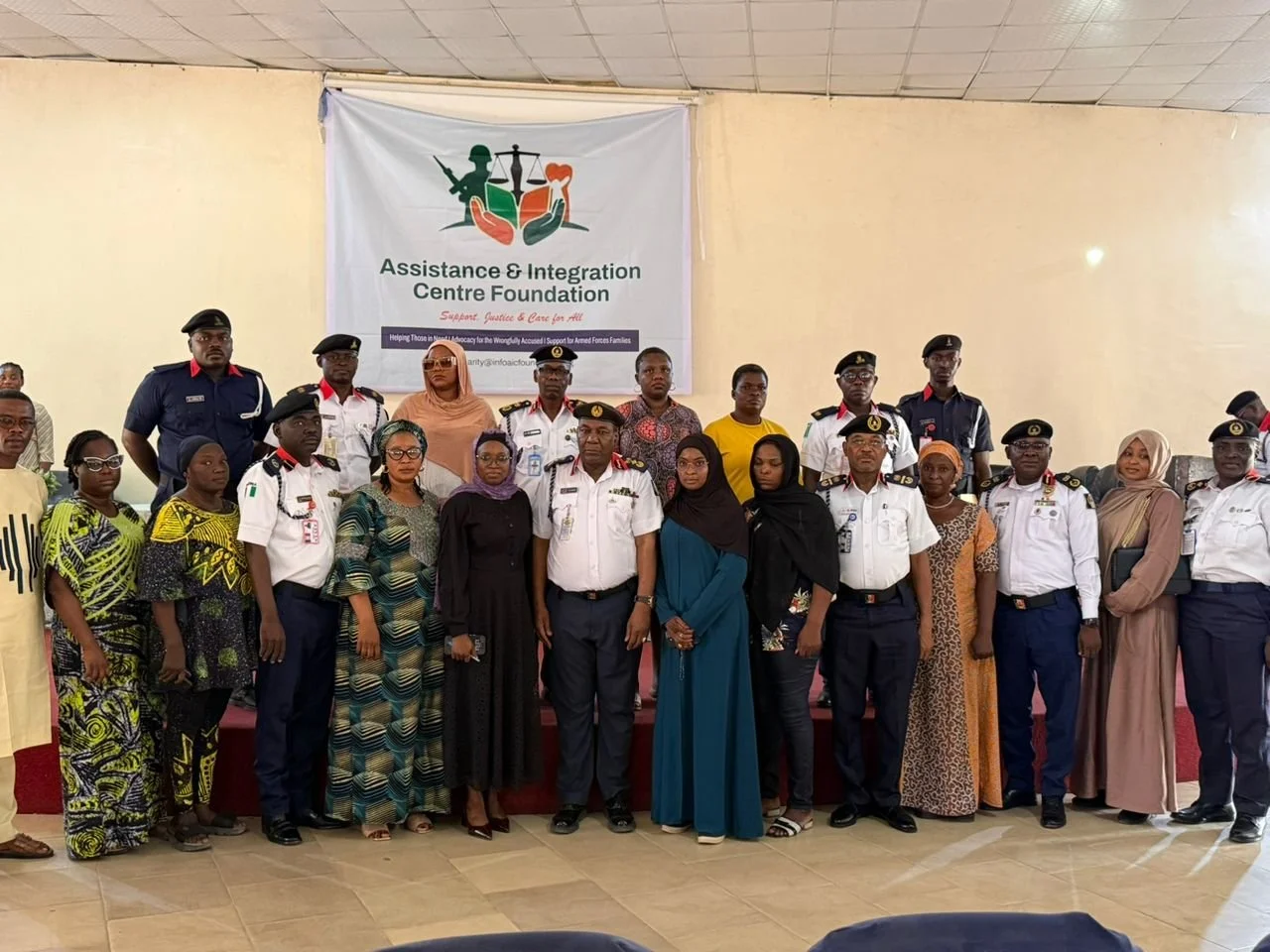 Group photo of people, including police officers and civilians, standing in front of a banner for the Assistance & Integration Centre Foundation during an event or gathering.